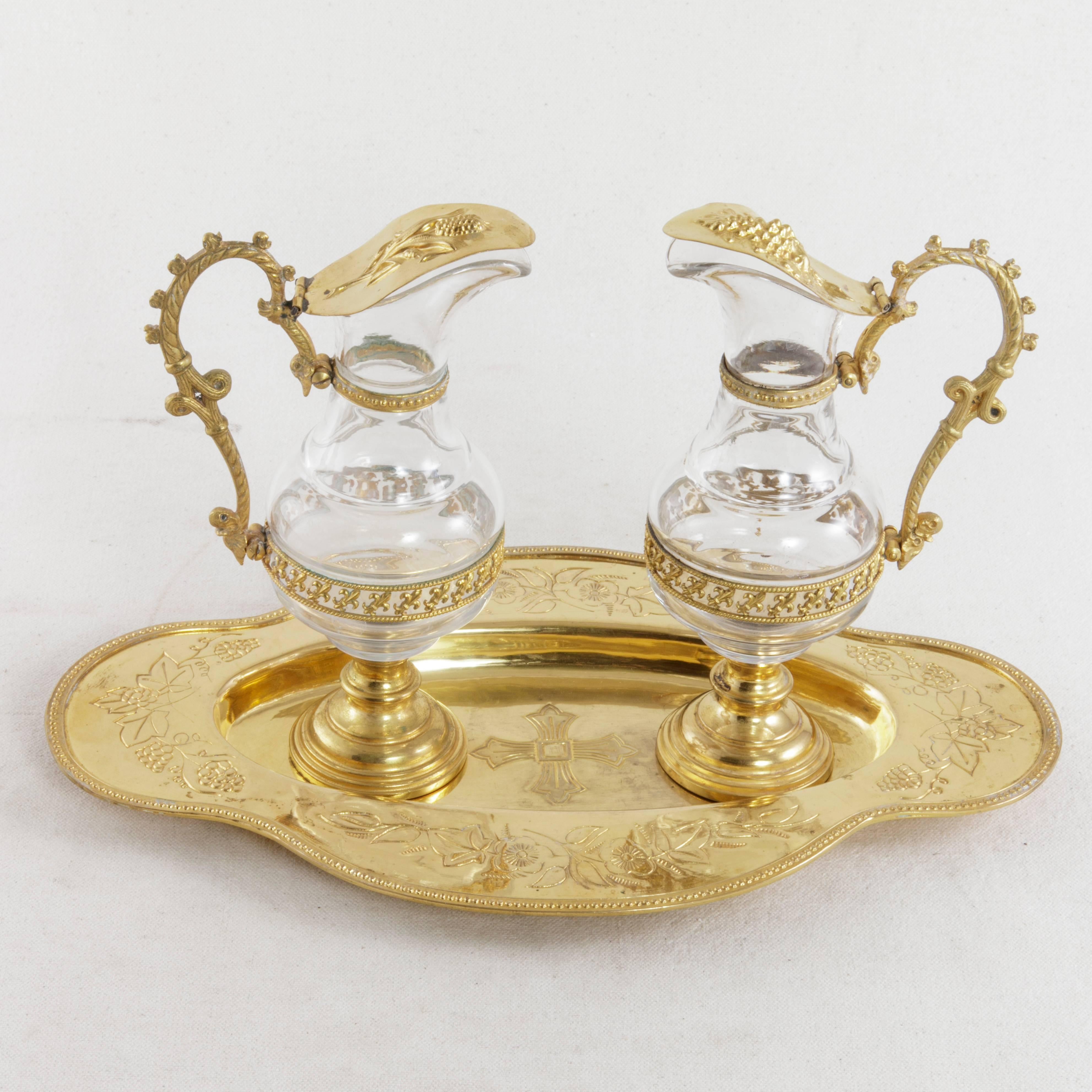 Originally used on the altar by a priest for consecrating wine for Holy Communion, this set of glass cruets from the early 20th century features gilded metal lids detailed with wheat on one and grapes on the other. A ring of fleur-de-lys on the