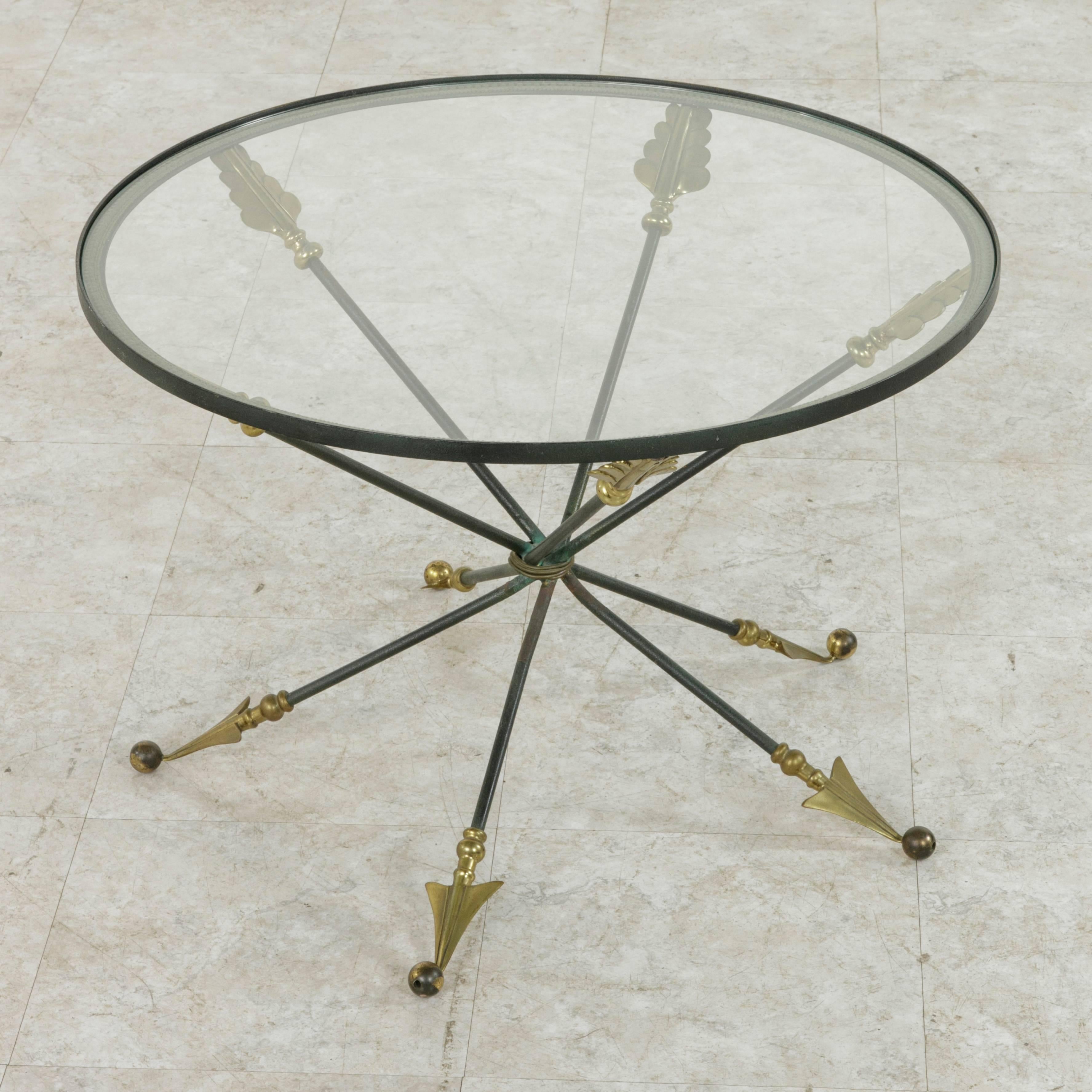 This midcentury French coffee table features a round glass top supported by a Directoire inspired bronze base with five crossed arrows bound together by a bronze ring. The aged verdigris patina of the base contrasts beautifully with the polished