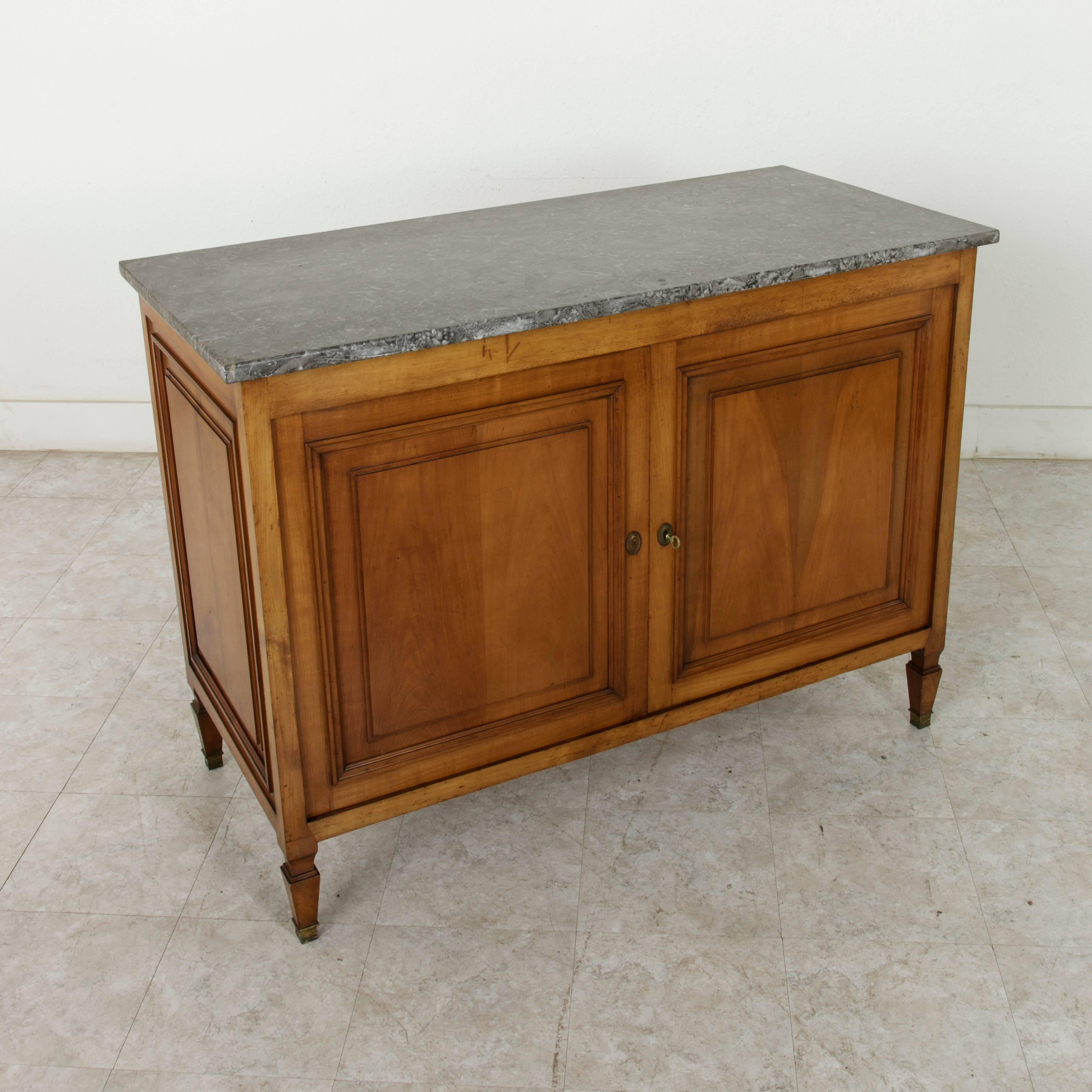 This circa 1900 French cherrywood Directoire style buffet rests on tapered feet finished with bronze sabots. It features raised panelled sides and two doors that open wide to reveal an interior with a single shelf and two drawers. The right hand