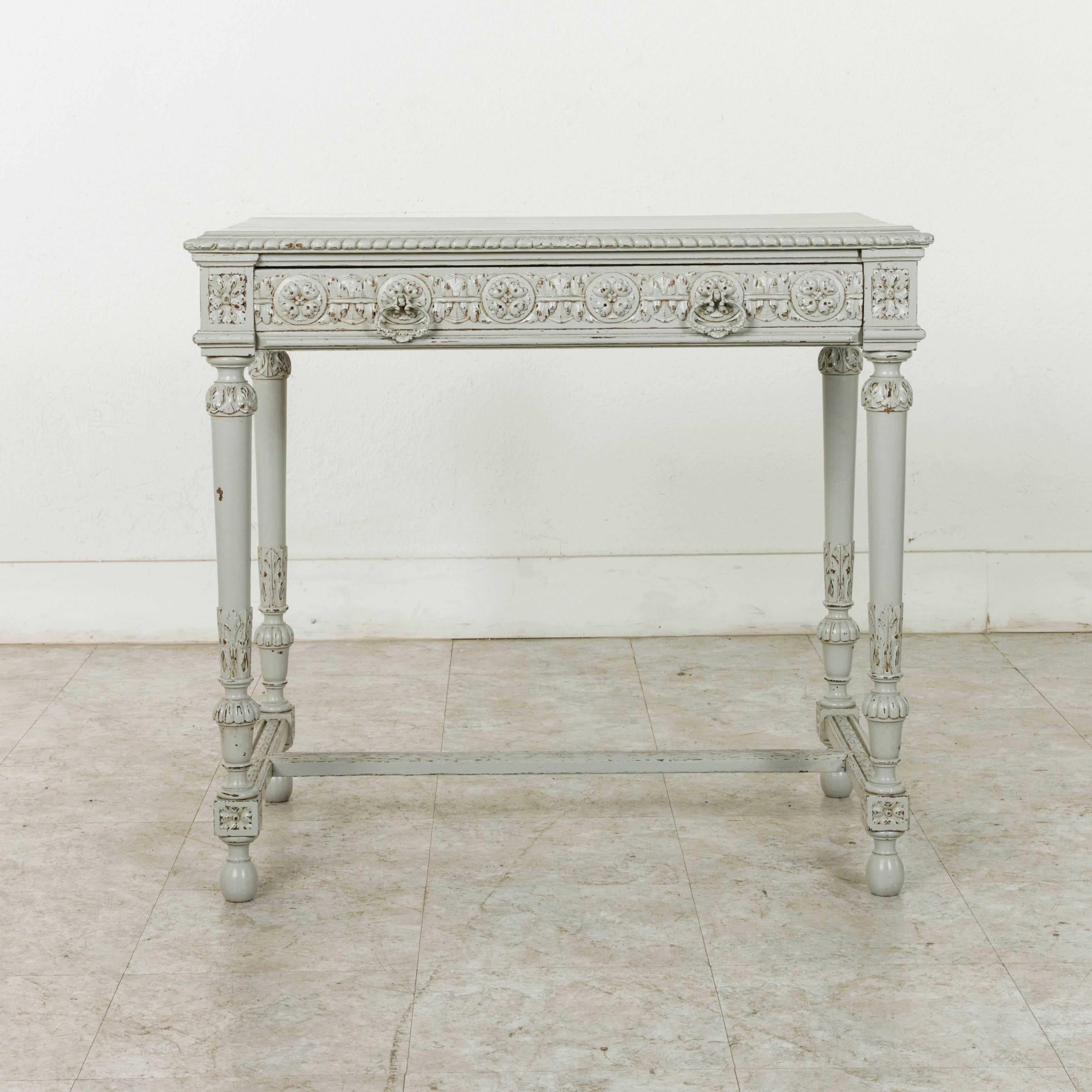 This late 19th century writing desk features intricate hand-carved Louis XVI motifs of rosettes and acanthus leaves and is finished on all sides. Painted in a classic Marie Antoinette grey, this desk has a single drawer fitted with two drawer pulls.
