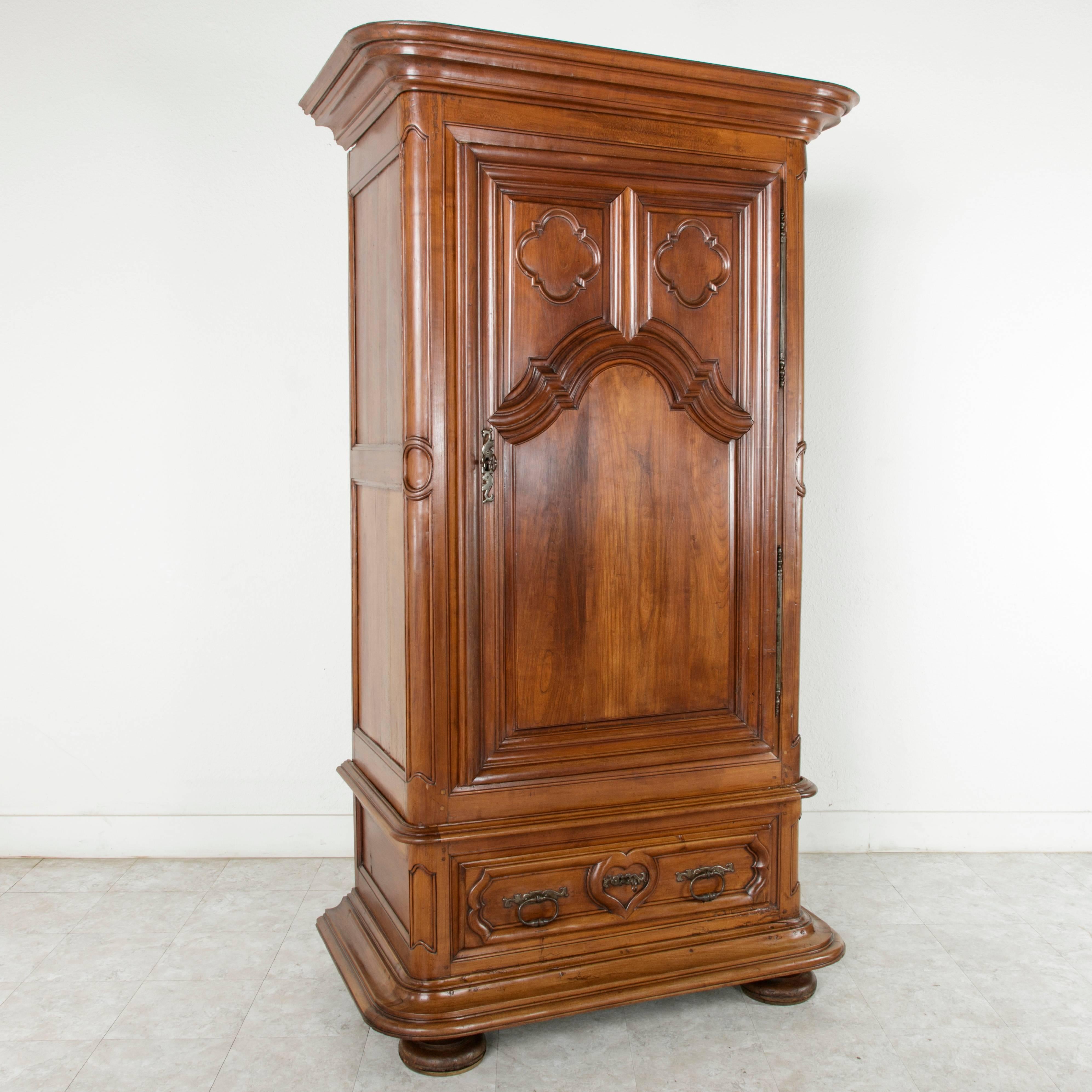 This exceptional 18th century walnut bonnetiere or armoire features hand carved deep relief panels with quadrofoils in its single door and a carved heart on its lower drawer. A classic piece in the Louis XIII style, this armoire rests on bun feet
