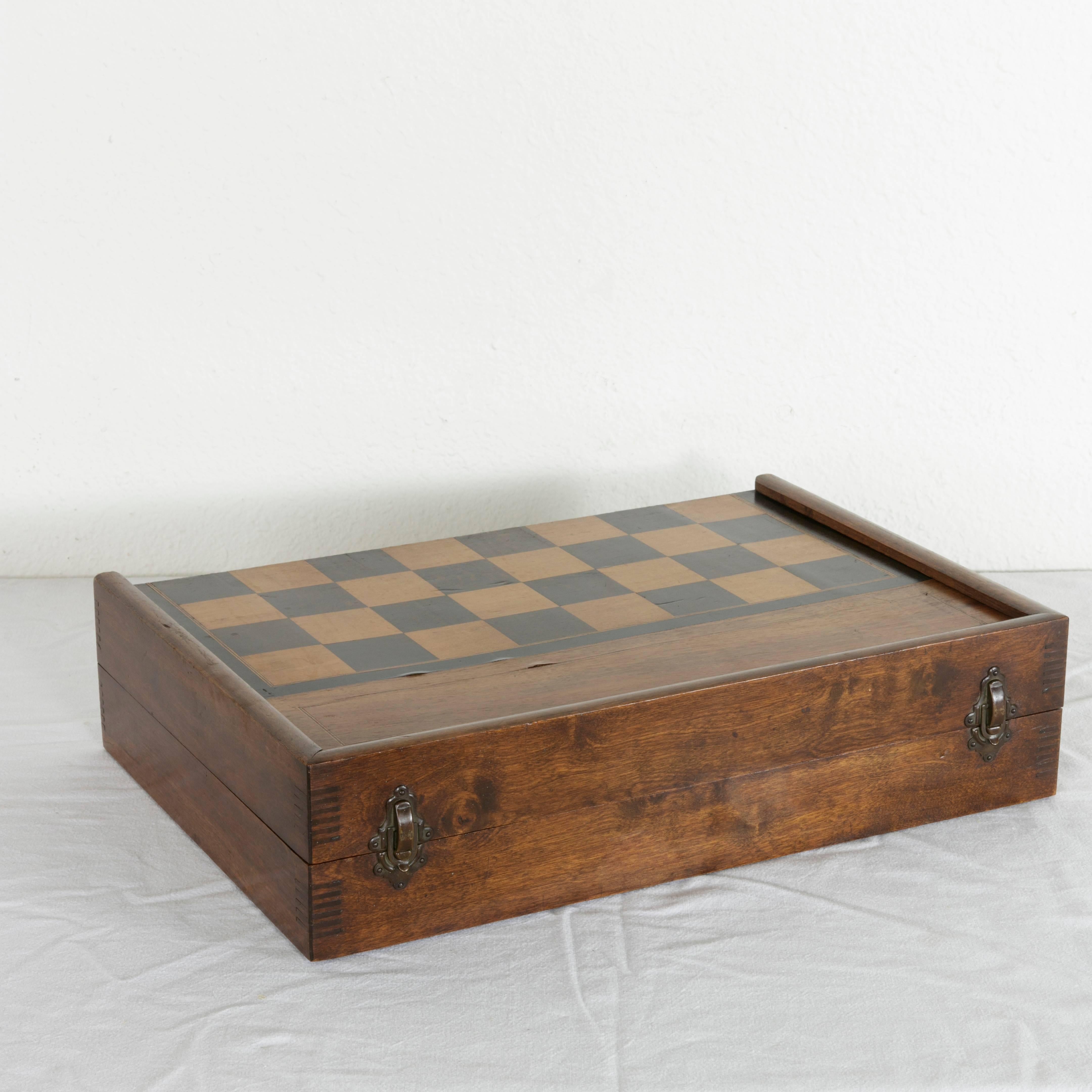 This early 20th century French parquetry game box includes hand carved chess pieces, 15 checkers or backgammon pieces, wooden dice, and two leather shakers. A handsome box with dovetailed corners and a rich patina, it is hinged in the middle to