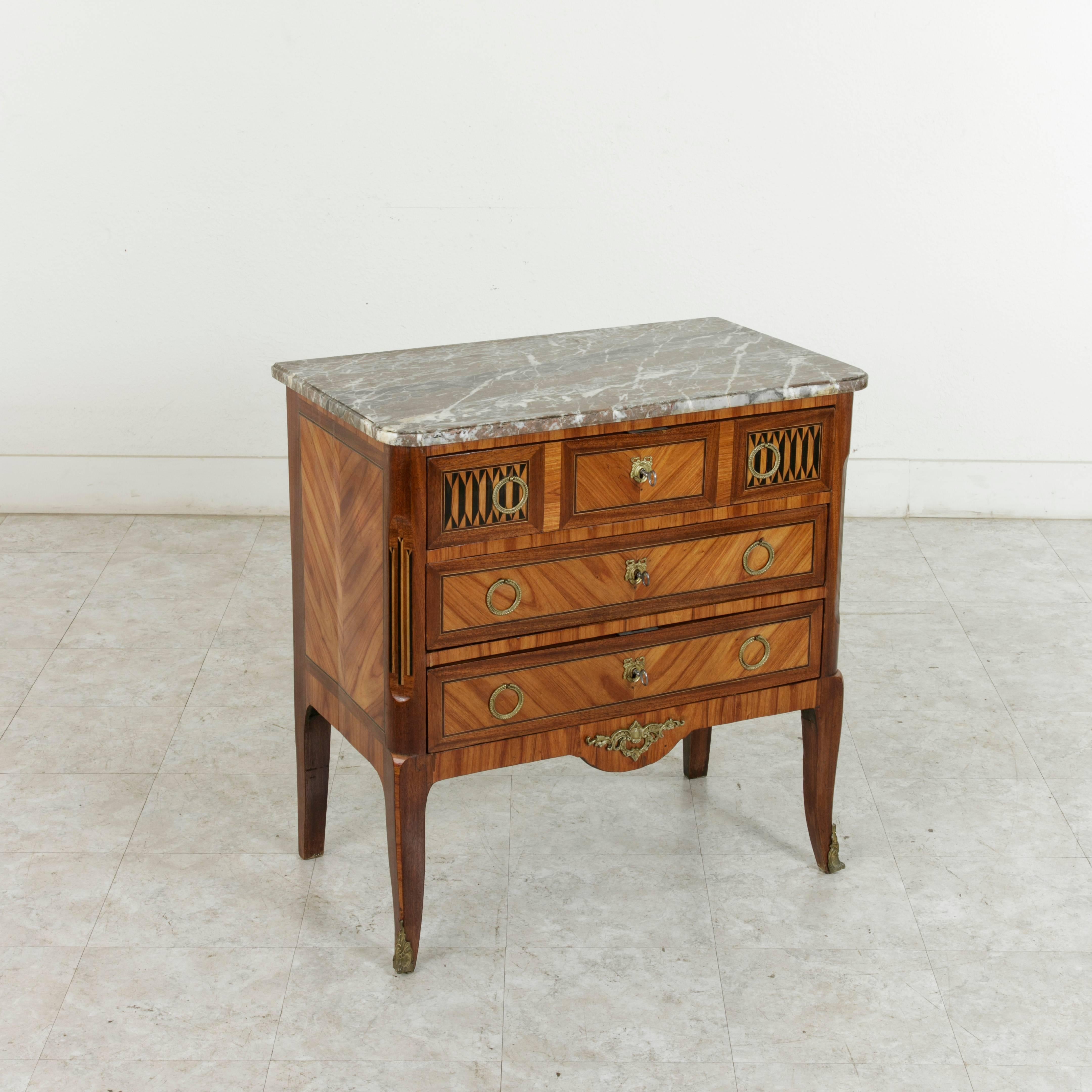 Unique for its small-scale of 30 inches in width and 32 inches in height, this Louis XV-Louis XVI Transition style commode or chest features exquisite marquetry work. Its three book matched rosewood drawers are enhanced by inlaid lemon wood and