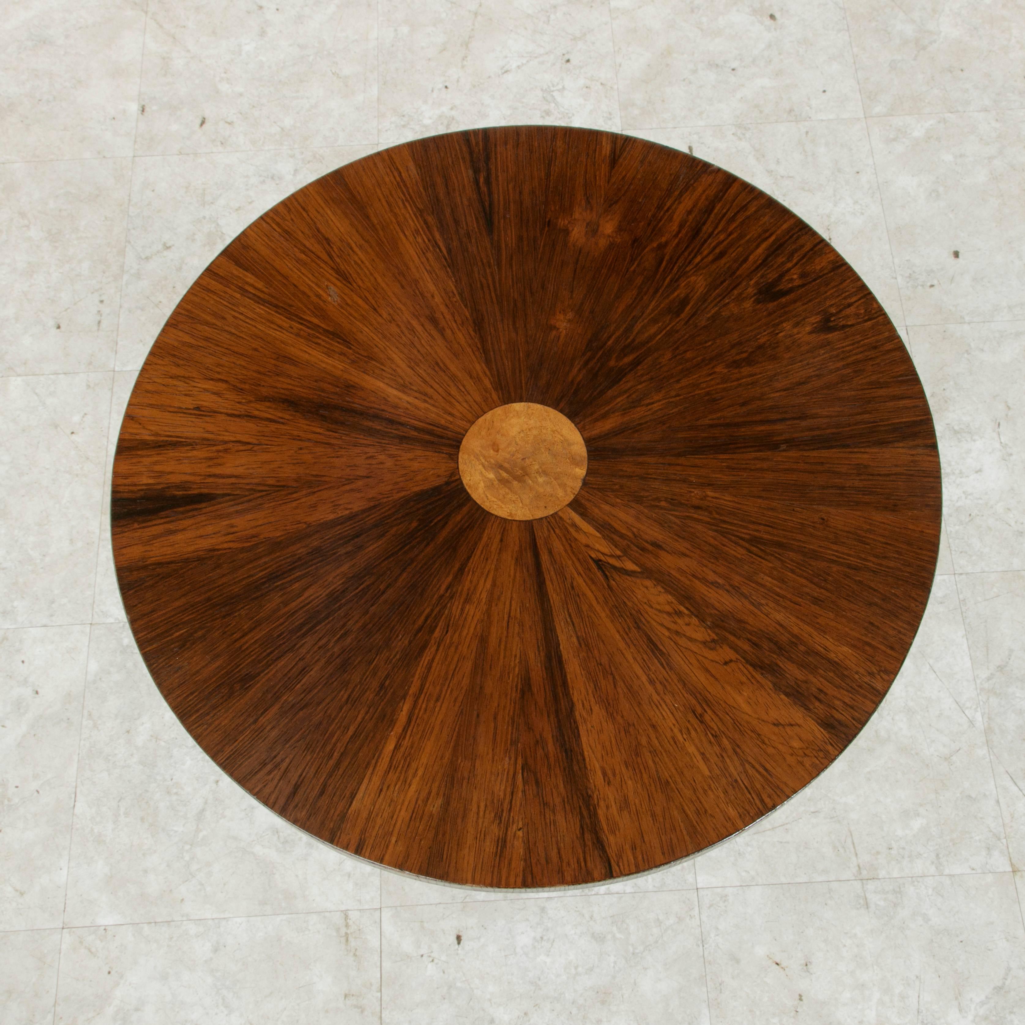 This early 20th century gueridon from the French Art Deco period features a palisander sunburst top with a central inlaid circle of burl walnut. The top is mounted on a unique four tiered pillar supported by a circular base. With its simple refined