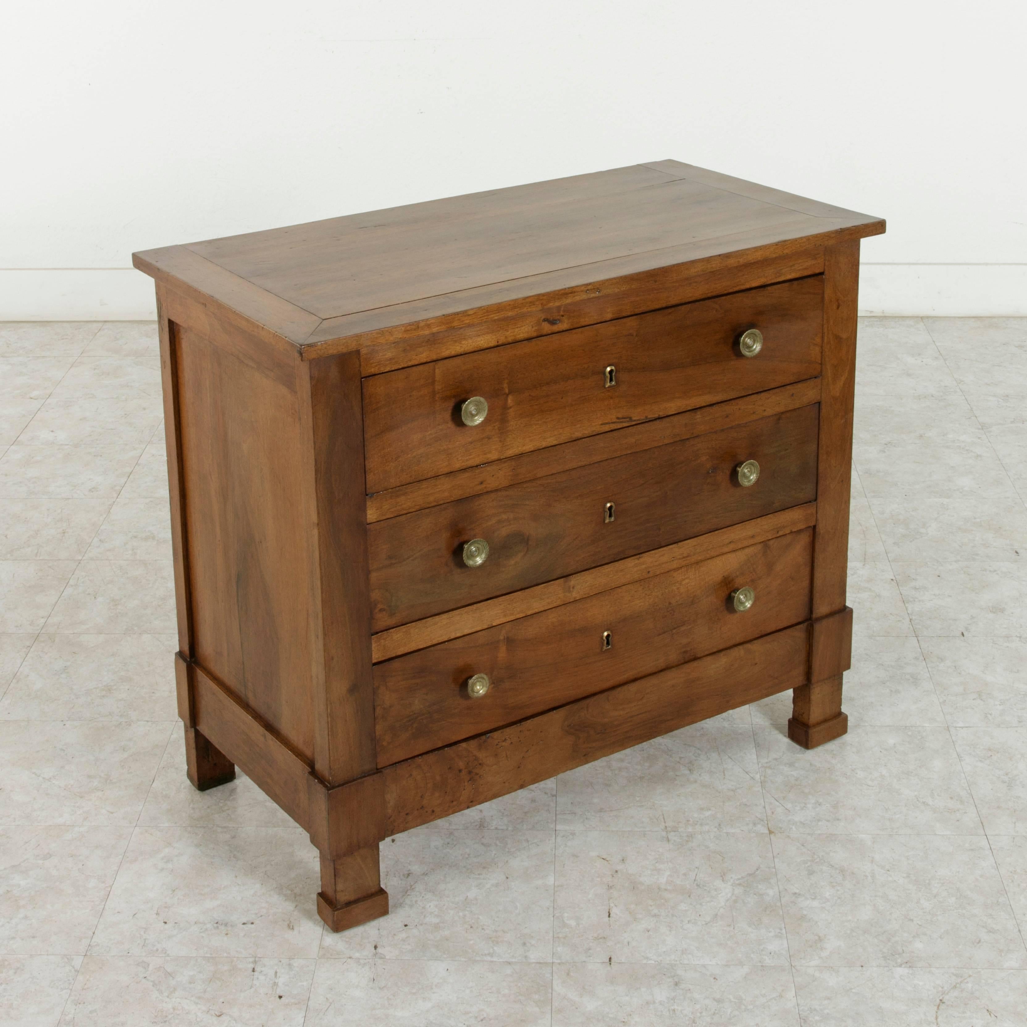 This late 19th century French walnut Empire style commode or chest features solid panel sides and clean, simple lines. The three drawers of dovetail construction are fitted with bronze drawer pulls and key entries. Unique for its size, this handsome