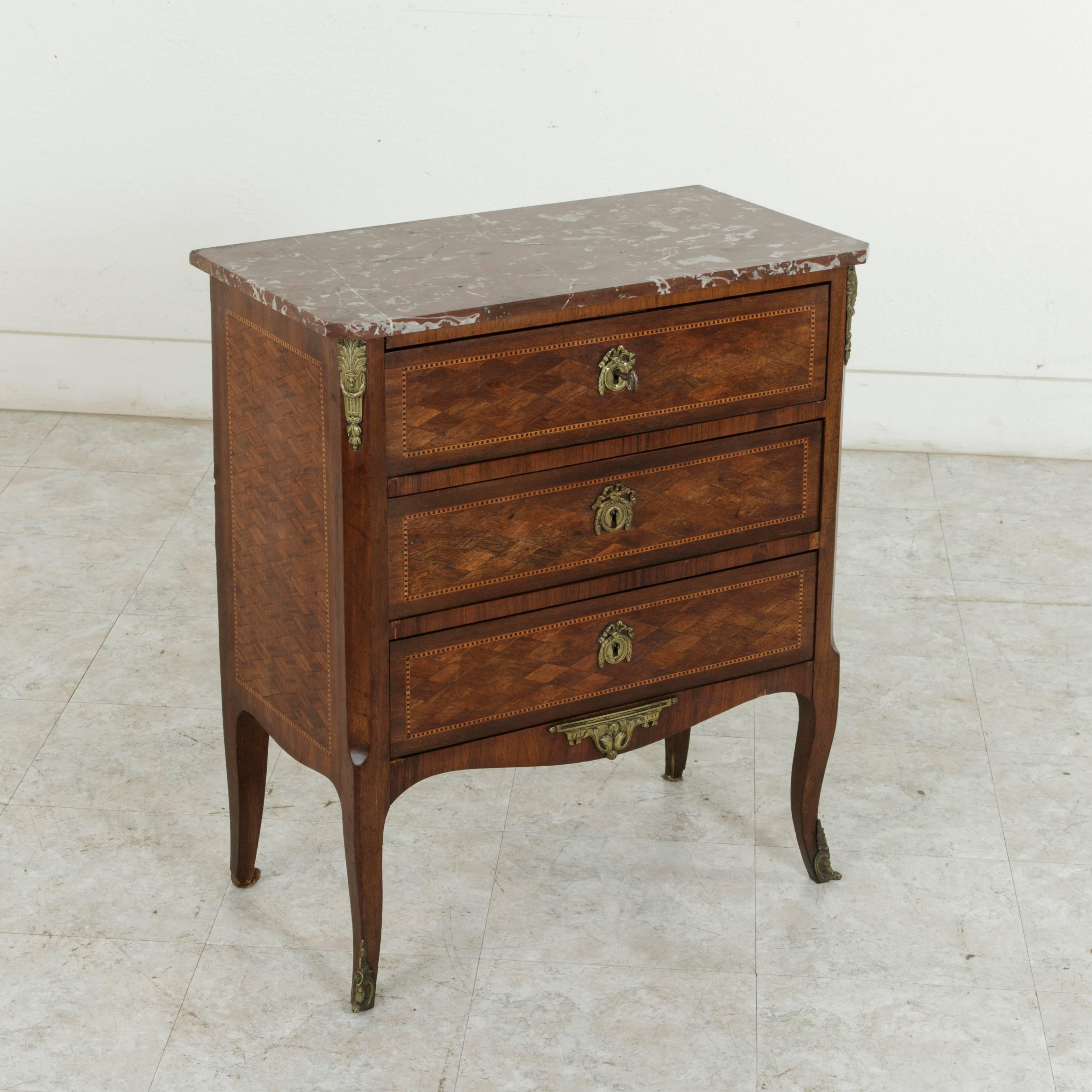 This small-scale French Louis XV-Louis XVI Transition style commode or chest features rosewood marquetry in a geometric diamond pattern on the front and sides with a striated border of rosewood and ebonized pear wood. Three drawers of dovetail