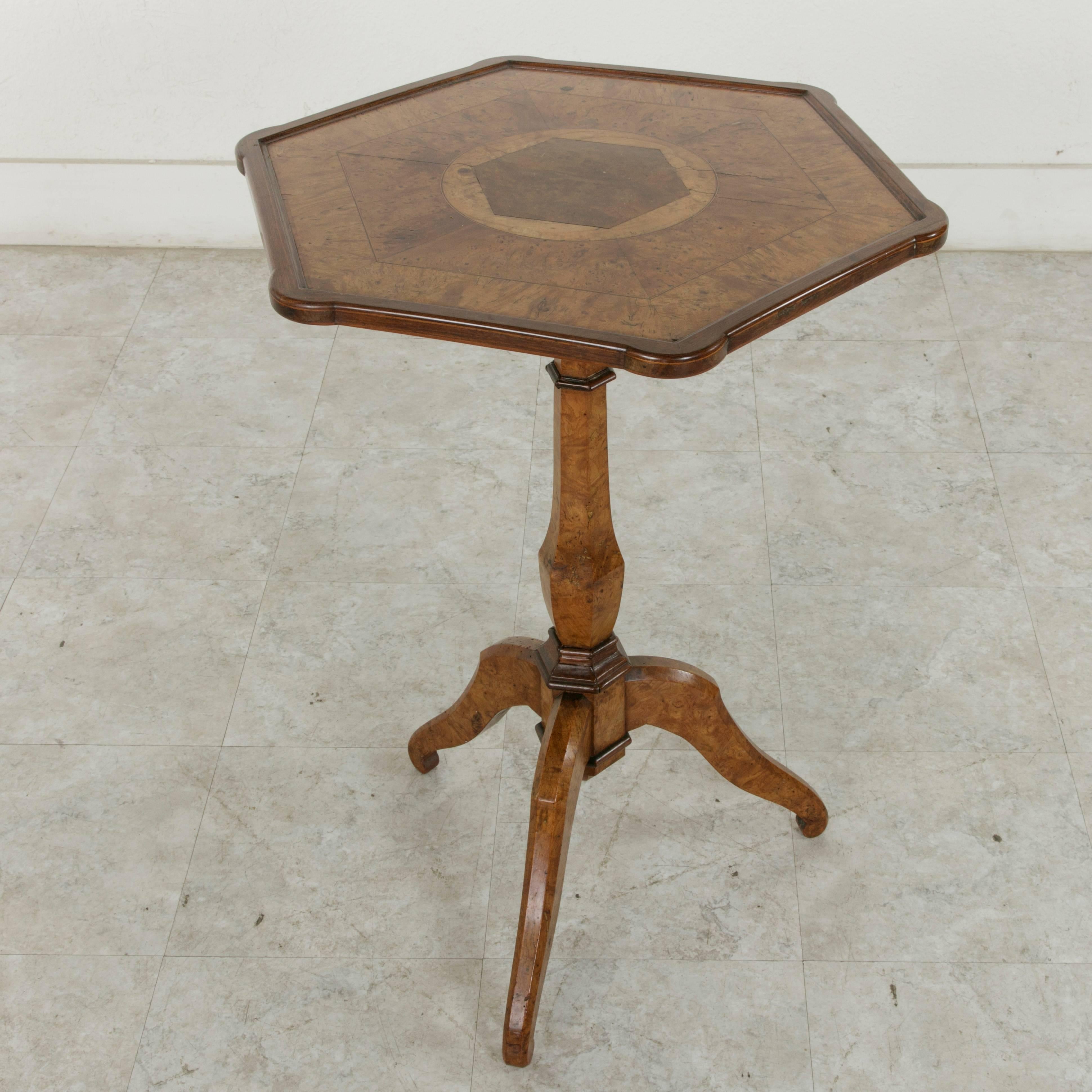 This French Charles X period pedestal table or gueridon circa 1820 features an hexagonal top with rounded corners constructed of walnut and burled elm. Fine lines of inlaid walnut and elm form concentric hexagonal rings on the top around the central