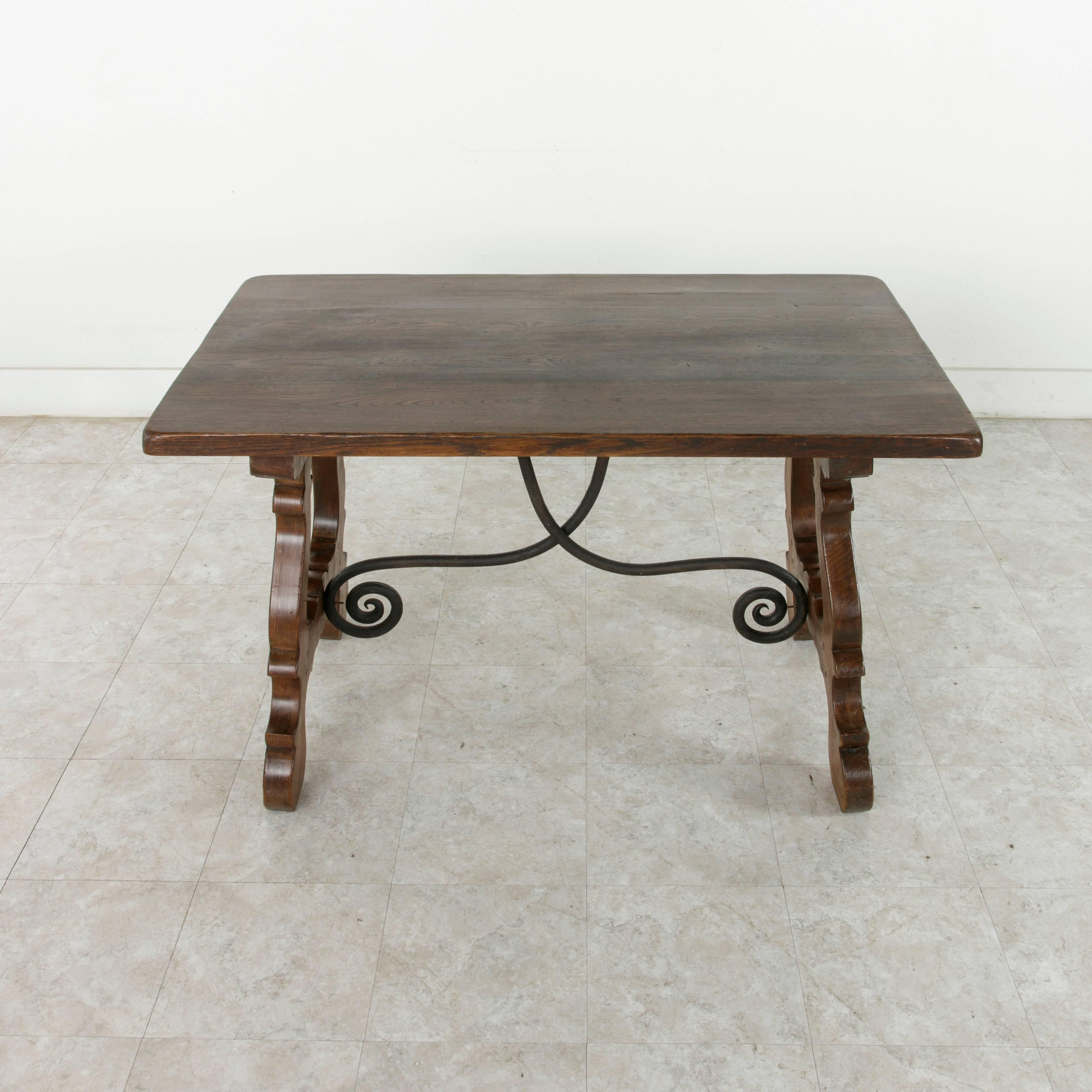 Found in Le Mans, France, this oak Spanish Renaissance style table features two gracefully carved legs joined by a hand forged iron stretcher finished with iron rosettes.  With a 47 inch length and 29 inch width, it is of an ideal size for a