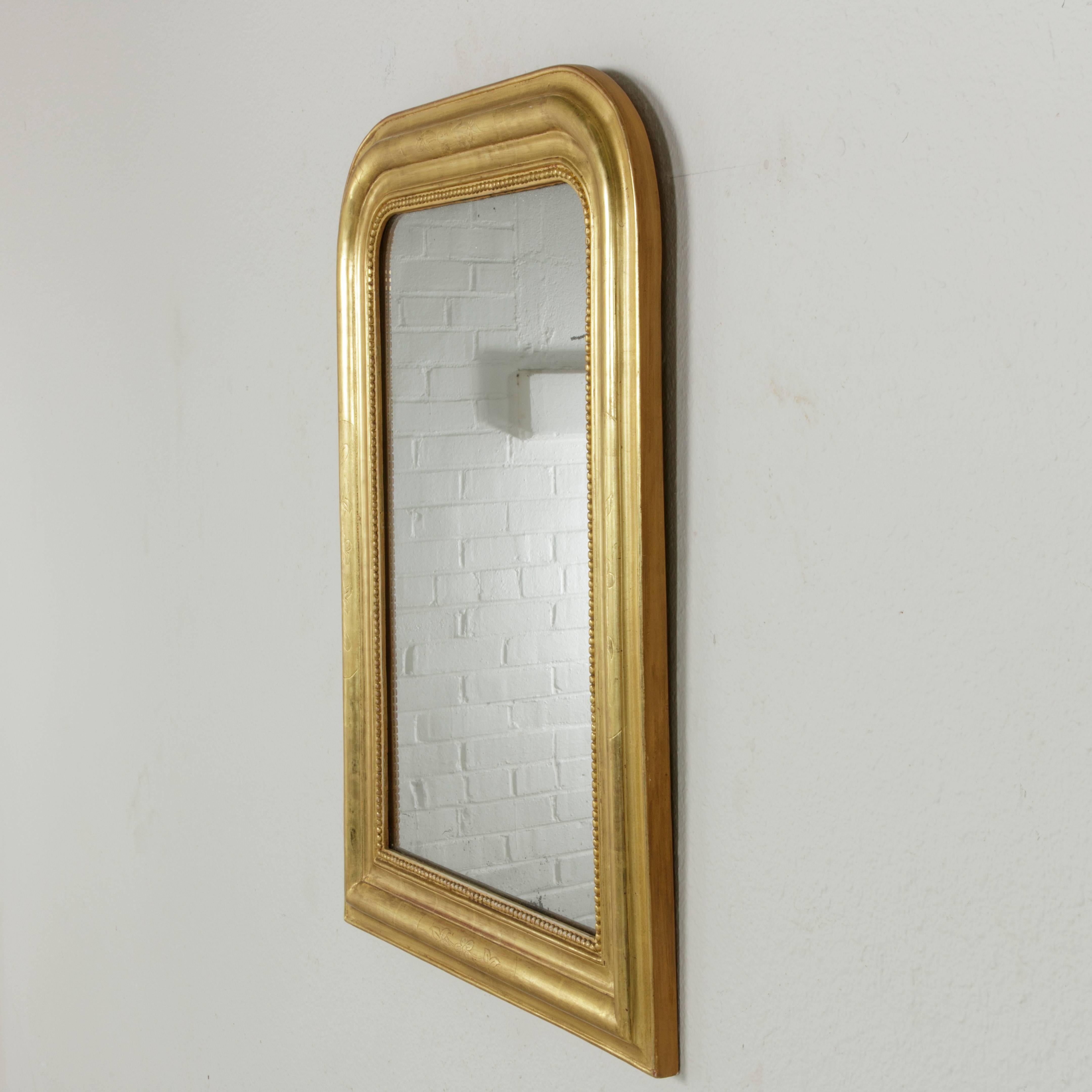 This small-scale 19th century Louis Philippe mirror with its flawless gilding and original mercury glass is an exquisite jewel. The giltwood frame features an inner border of fine beading and the pillow frame is detailed with subtle incising of