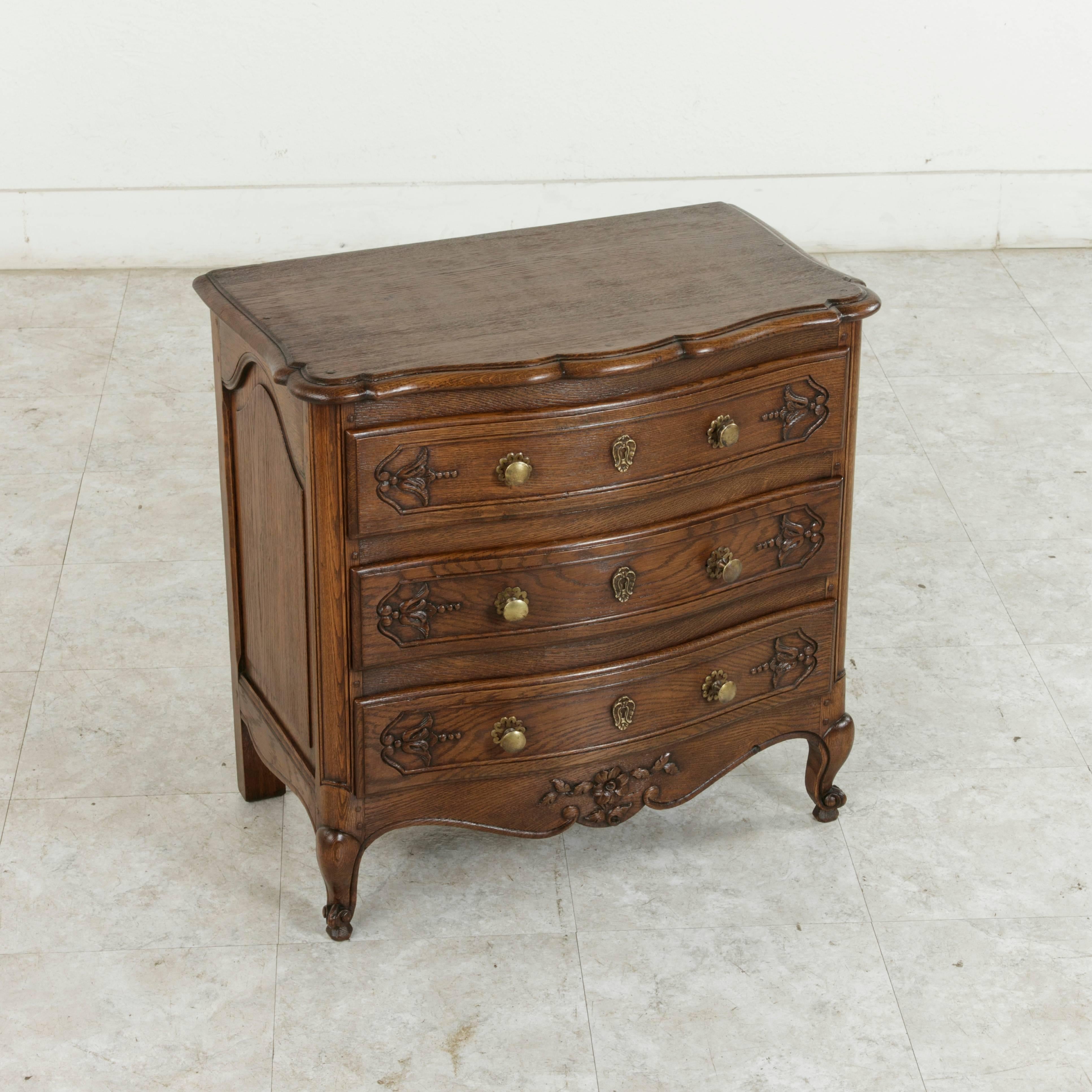 This small-scale French Louis XV style chest or nightstand from the early 20th century is made of hand-carved oak and features a bow front bevelled wood top, and hand pegged construction around its solid panel sides. Carvings of a floret with