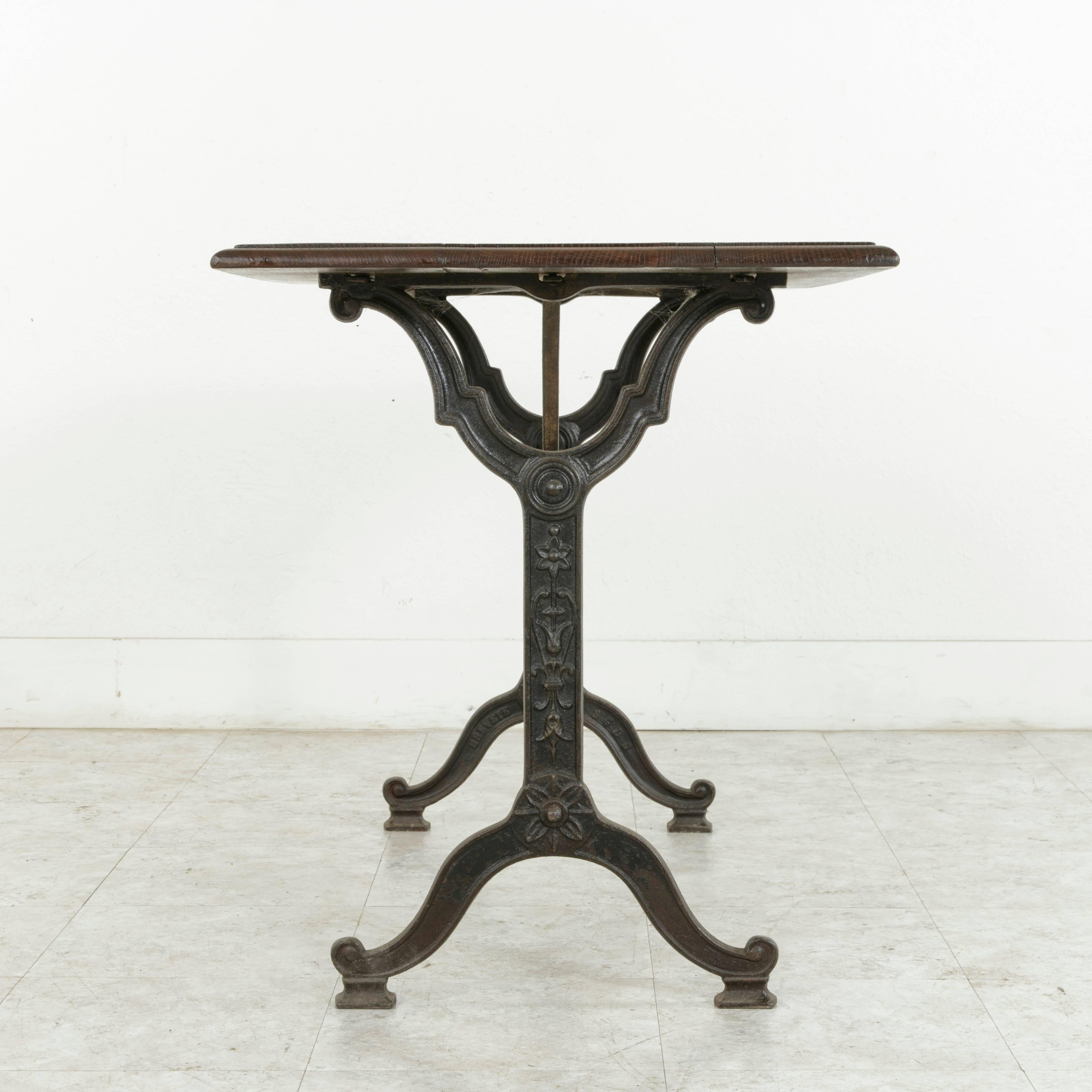 Originally used in a French brasserie around the turn of the 20th century, this Art Nouveau period bistro table or cafe table features a cast iron base and a beveled oak top constructed from three planks. The iron base of the piece is adorned with