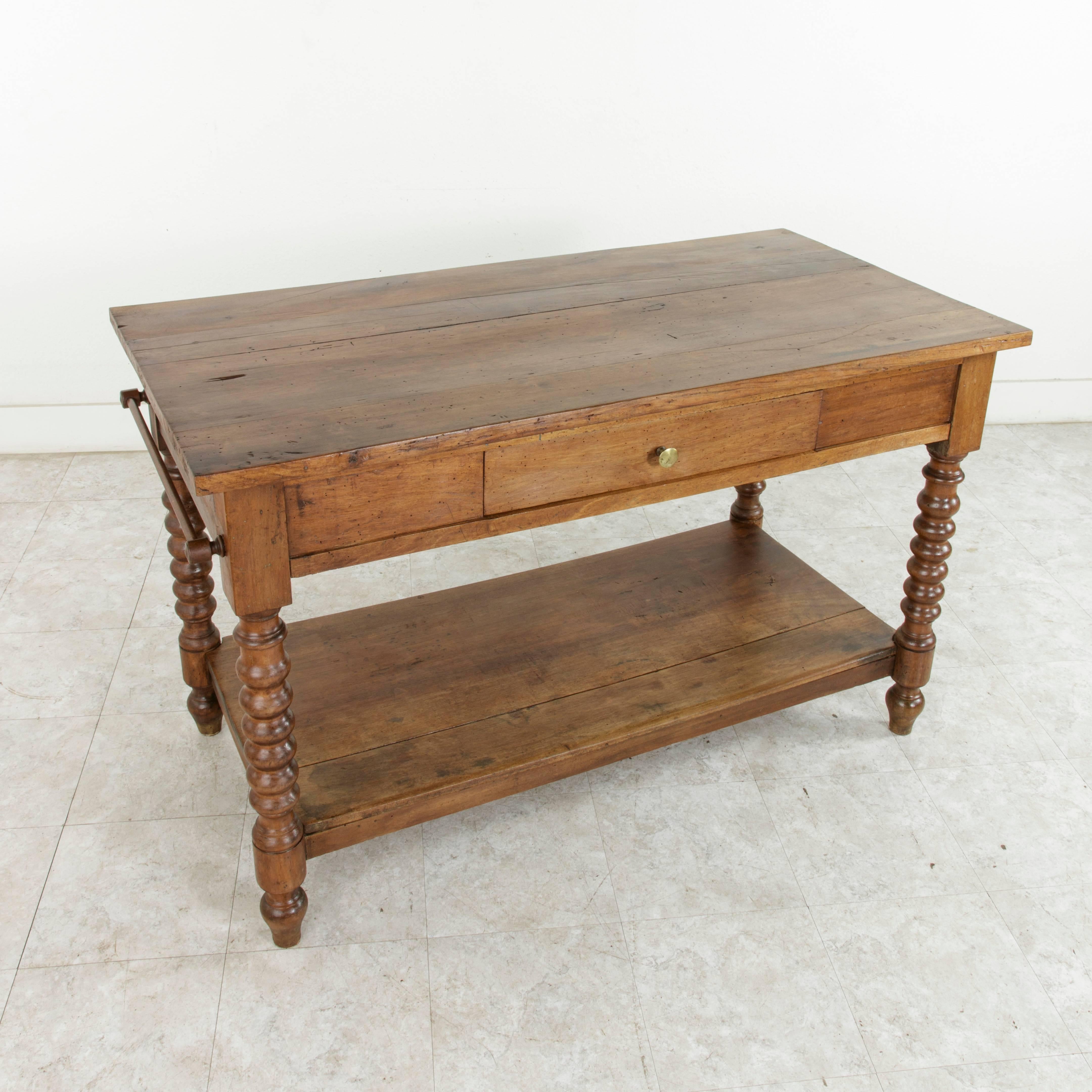 Originally used in a French fabric store to lay out and cut fabric in the 19th century, this solid walnut fabric presentation table rests on turned legs which support its lower shelf. A single dovetailed drawer on one side once held scissors and