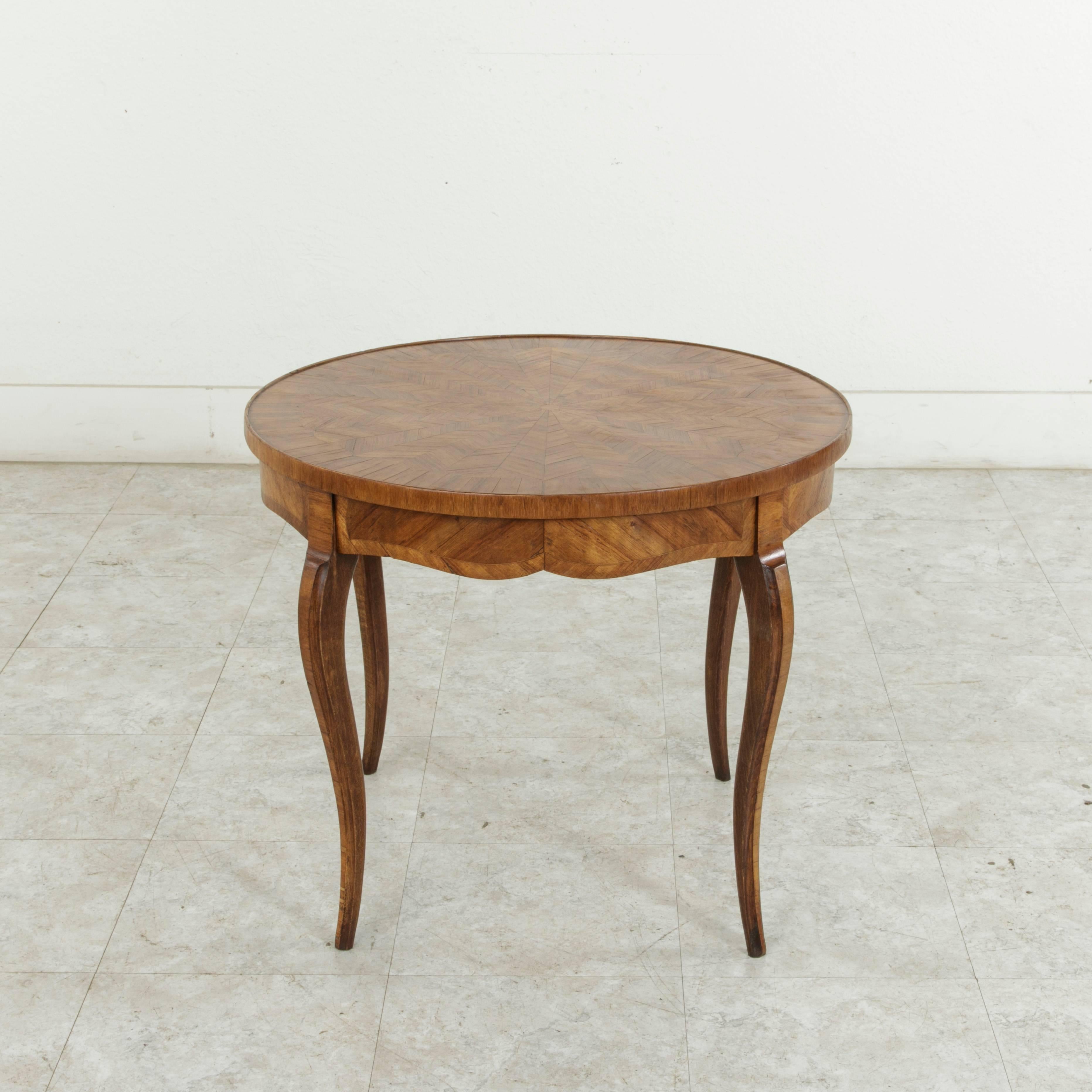This early 20th century French walnut marquetry coffee table features a banded round top inlaid with a geometric sunburst pattern. Gently curved cabriole legs complete the look. Ideal as a coffee table or cocktail table for small scale living, circa