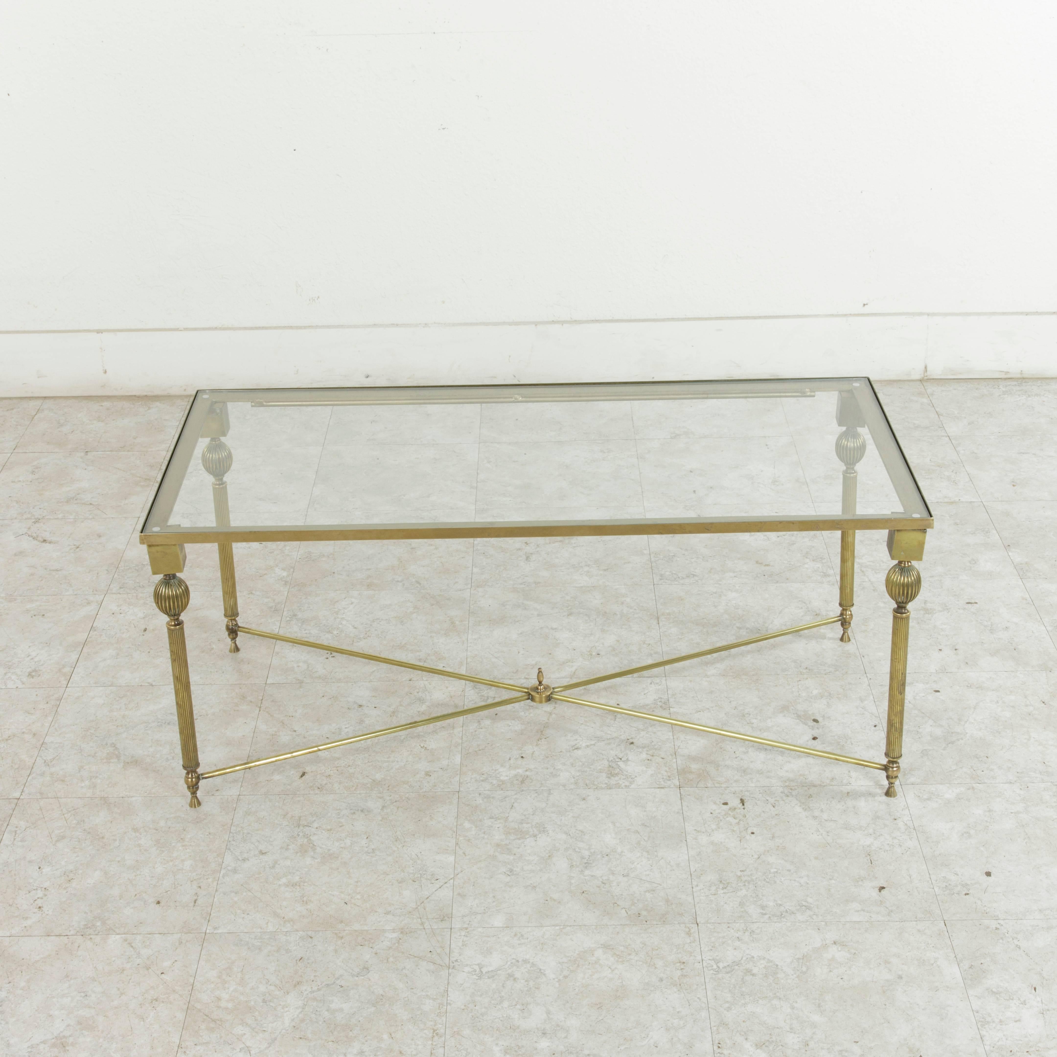 This midcentury French bronze coffee table attributed to Maison Jansen features elegant Louis XVI inspired fluted legs and an X-stretcher with a central finial. Finished with a glass top, this piece blends beautifully with both contemporary and