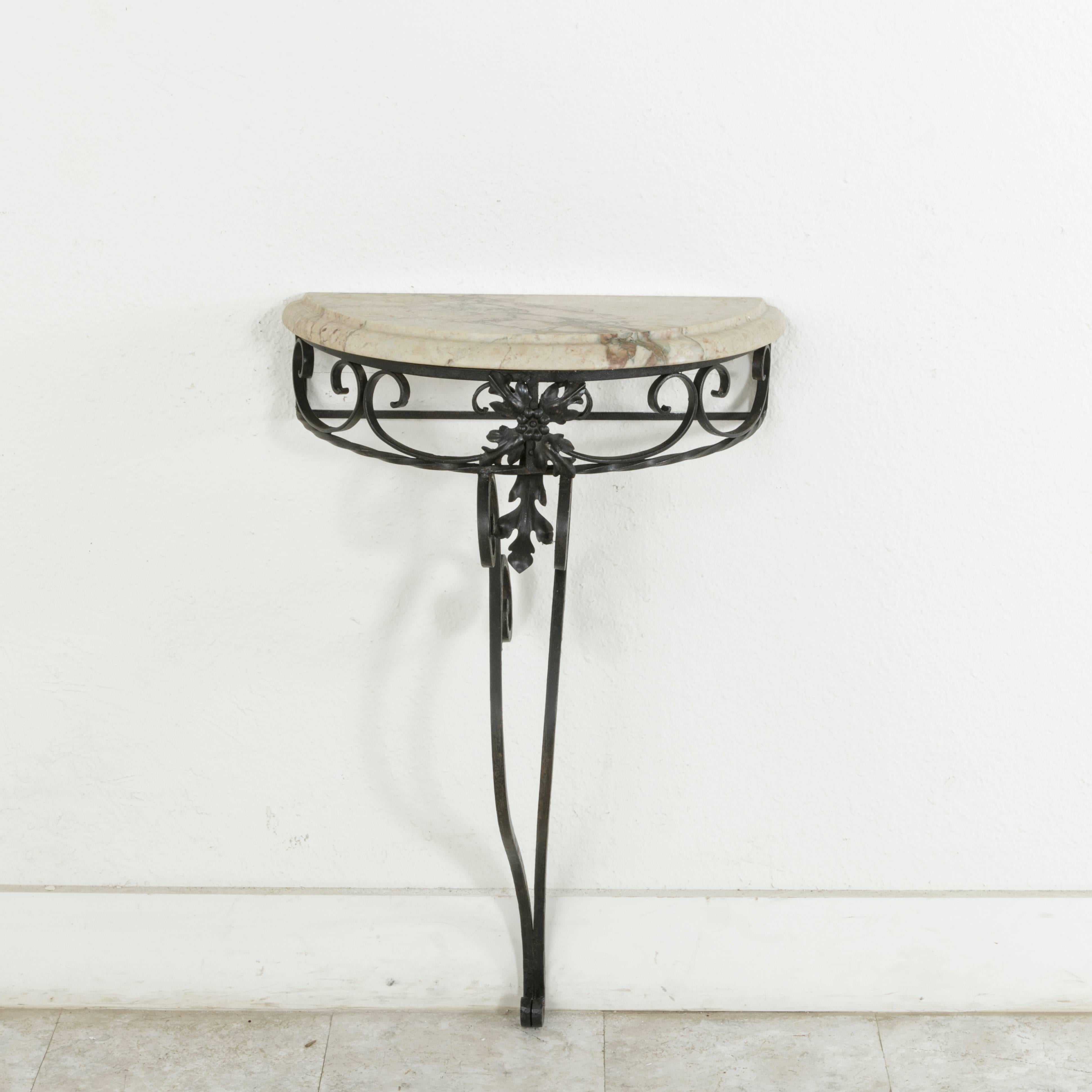 This small-scale mid-20th century French iron demilune console table features a central scrolled leg crowned with stylized acanthus leaves. A bevelled marble top completes the look. Mounted against a wall, this console table would be ideal in a