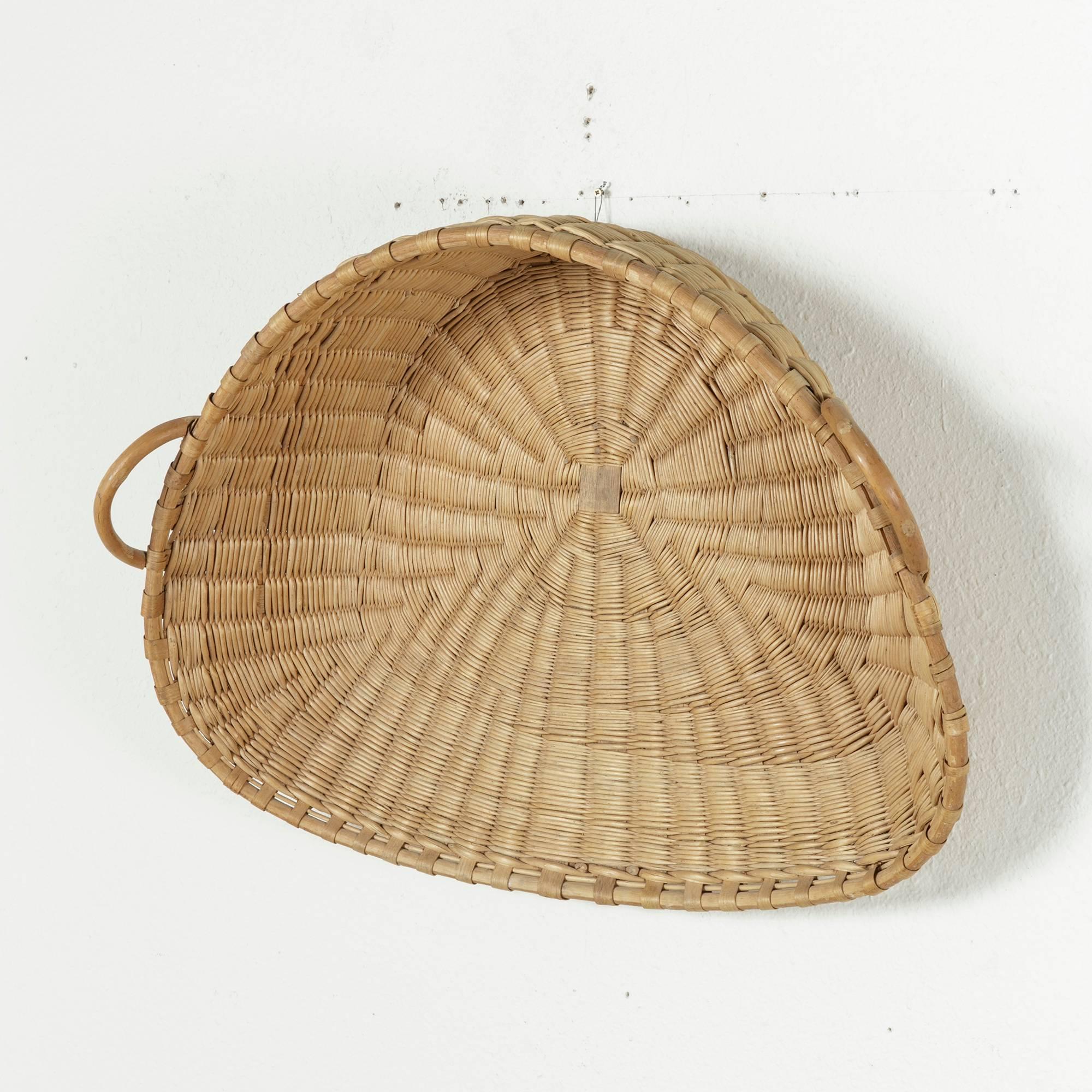 This exquisite 19th century handwoven French winnowing basket with wooden handles is in pristine condition. It was originally used to separate the wheat from the chaff by holding the flat side of the basket against one's stomach and tossing the