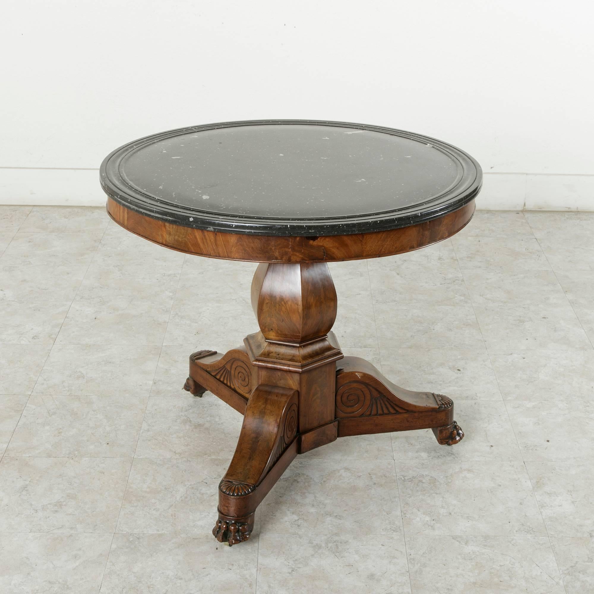 This mid-nineteenth century French Restauration period flamed mahogany gueridon rests on a tripod pedestal with claw feet and casters. Its black and white soapstone top features a multi-beveled edge. This circa 1850 piece is of an ideal size as