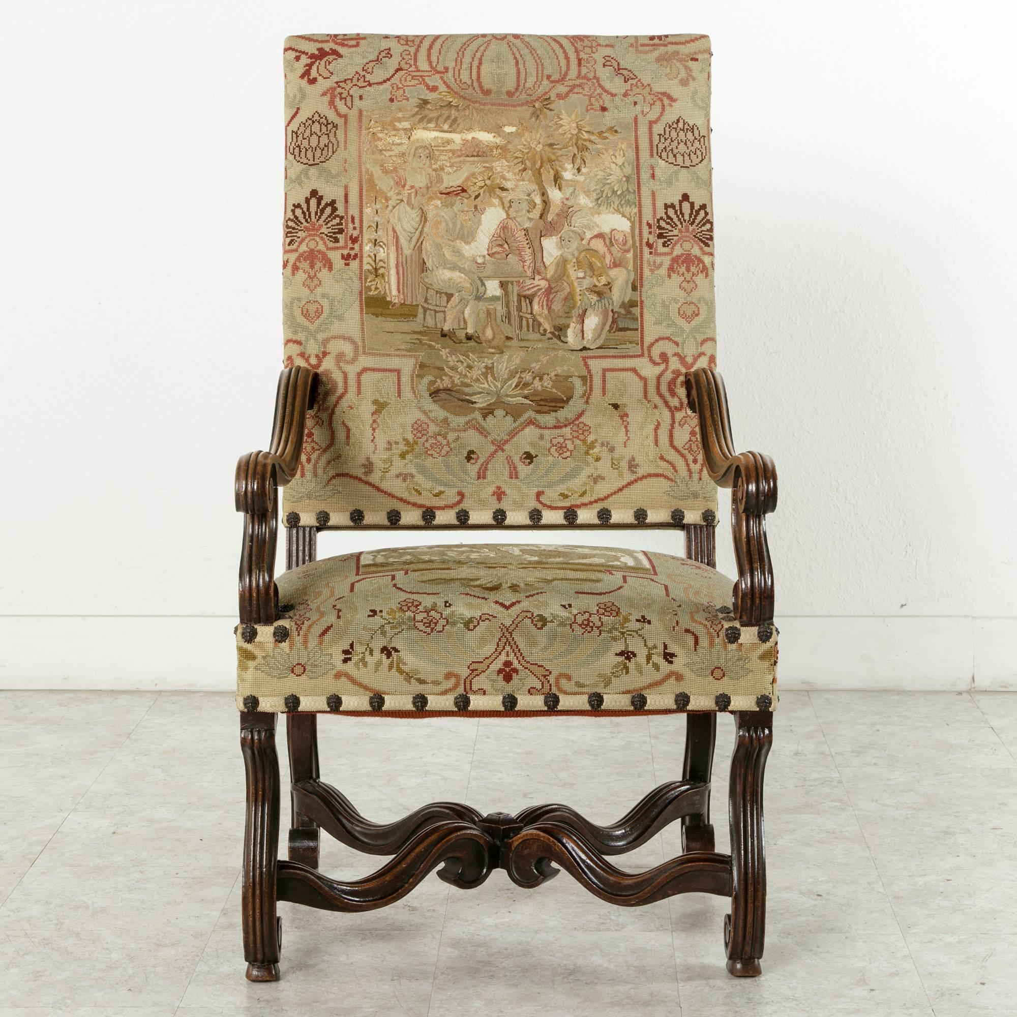 This nineteenth century hand carved walnut armchair in the Louis XIV style features fluted arms and legs.  Its four curved fluted stretchers extend from each leg to meet in the center, providing extra strength and support to the frame.    The