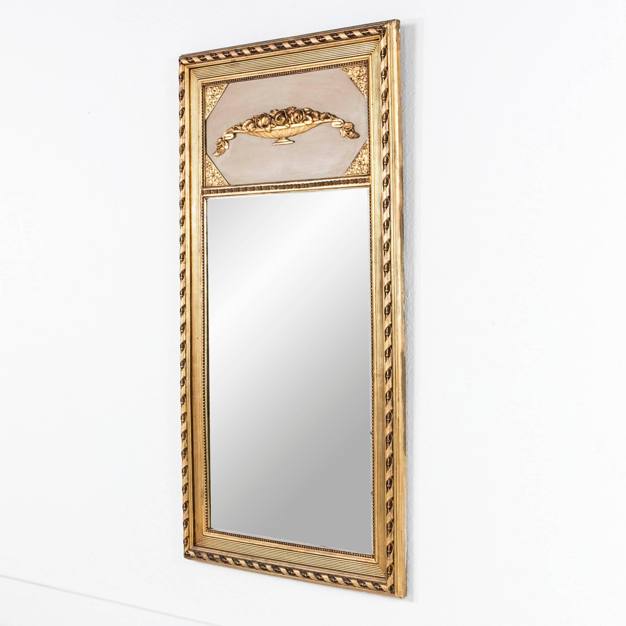 This Art Deco era giltwood trumeau mirror features an unusual elongated Art Deco interpretation of the Classic Louis XVI urn motif. The warm neutral background color of the trumeau will work well with most palettes, while the simple ribbon border on