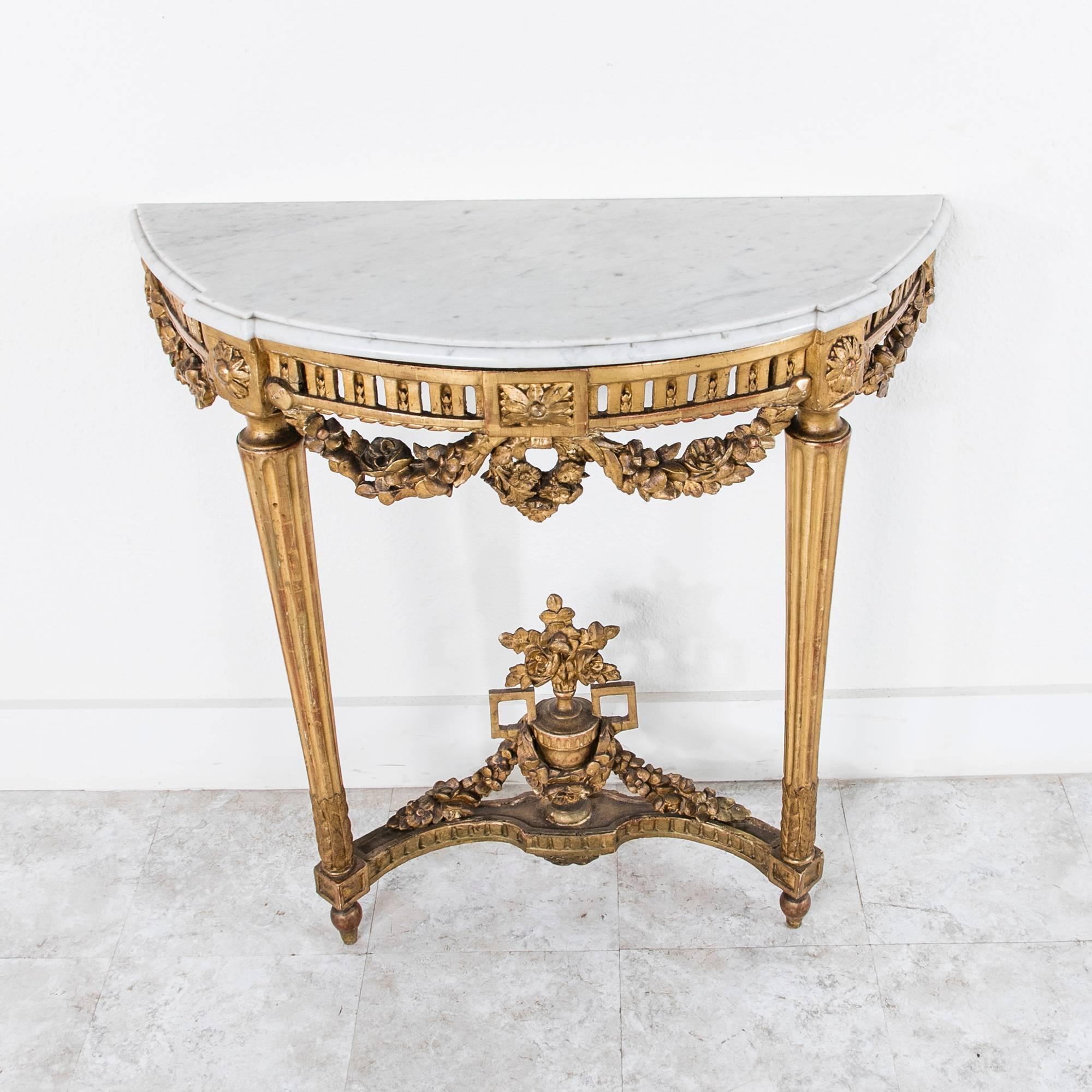 This extremely fine example of Louis XVI design was created in the late 18th century. Its beautifully carved giltwood apron features a draped, festooned garland and central wreath. Elegant slim fluted legs lead to a lower transom with a tall and