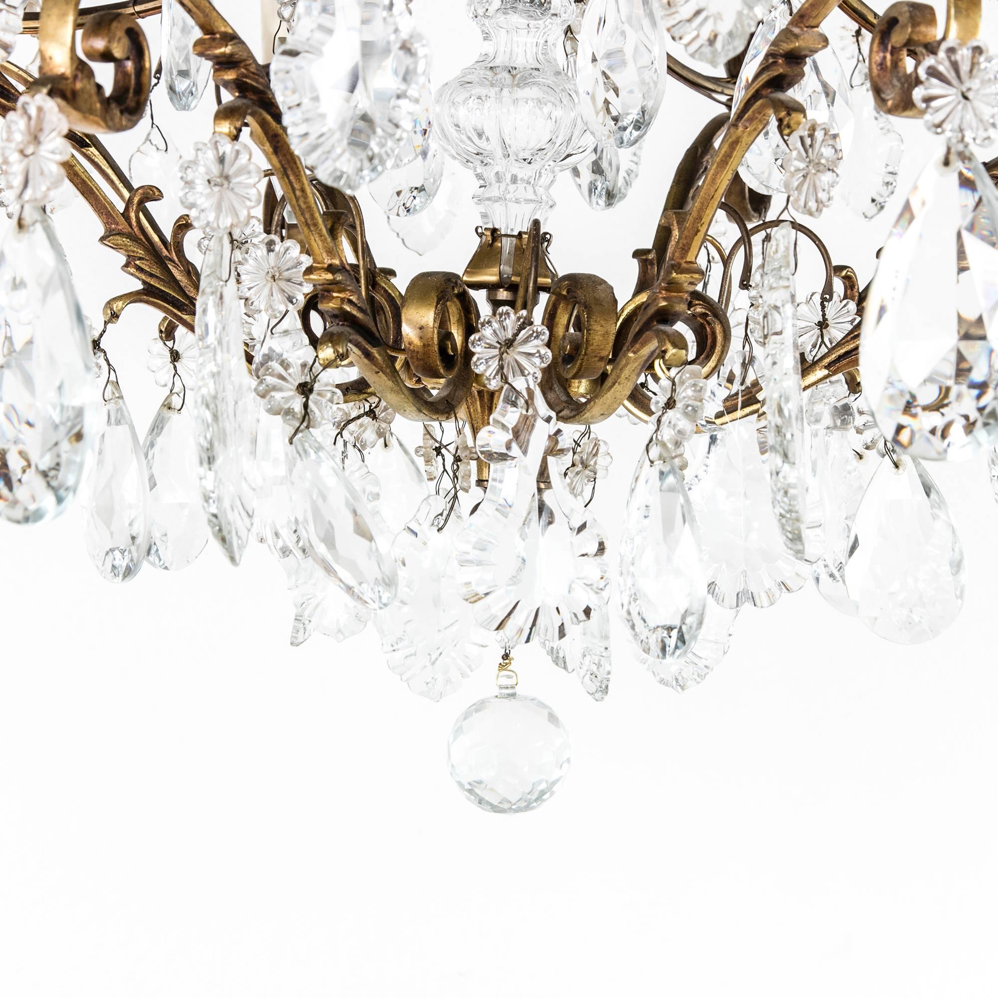 This beautifully patinated gilt bronze chandelier features scrolling acanthus leaves on its arms draped in crystal pendalogues which mirror its curvilinear form. Two additional rows of eight arms each holding large cut crystal teardrops with floral
