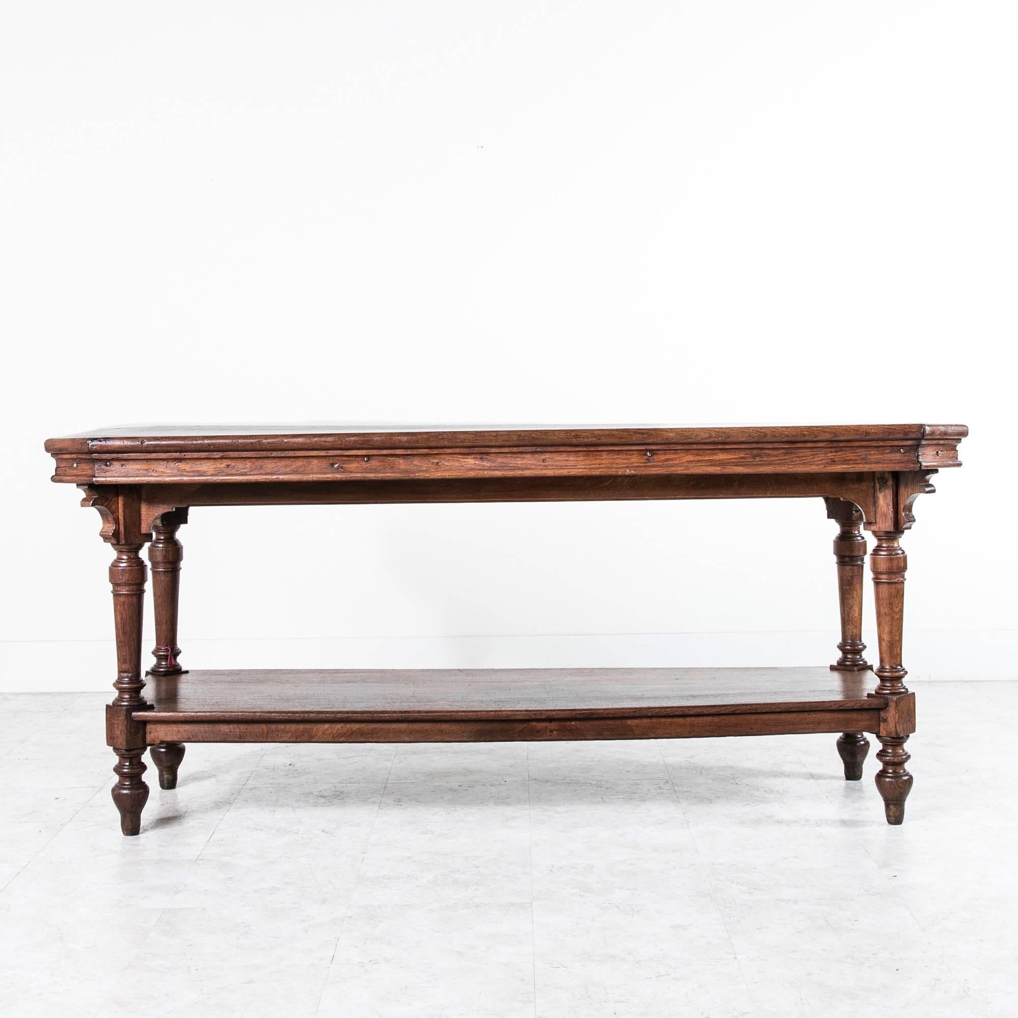 This large scale warm French oak fabric presentation table features unusual diagonal corners. The large lower shelf is perfect for showing off kitchen collections such as copper or baskets. This piece was originally used in a fabric shop for