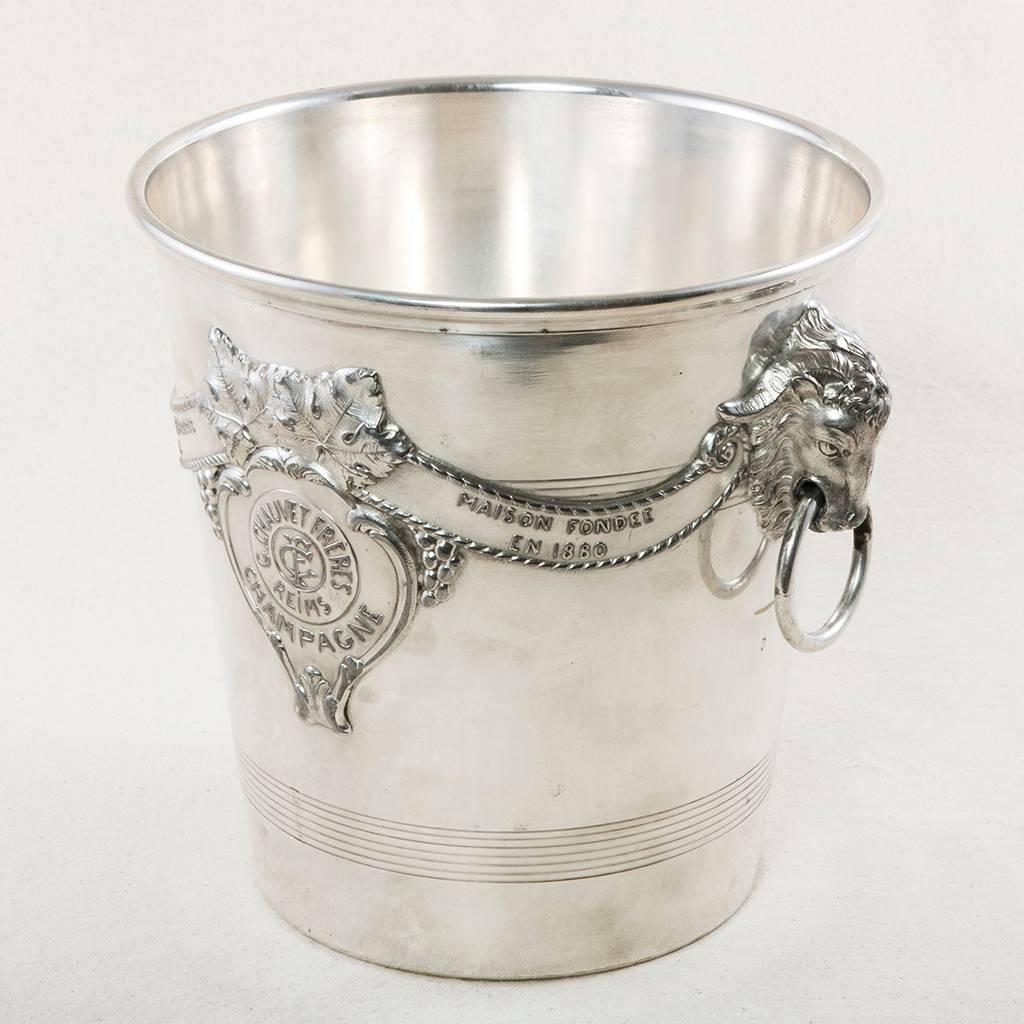 This exceptionally bright silver plate champagne bucket features ram's head handles and the label of the champagne house in Reims, France, founded in the year 1880.
  Three silver hallmarks on bottom. Please contact French Metro Antiques for