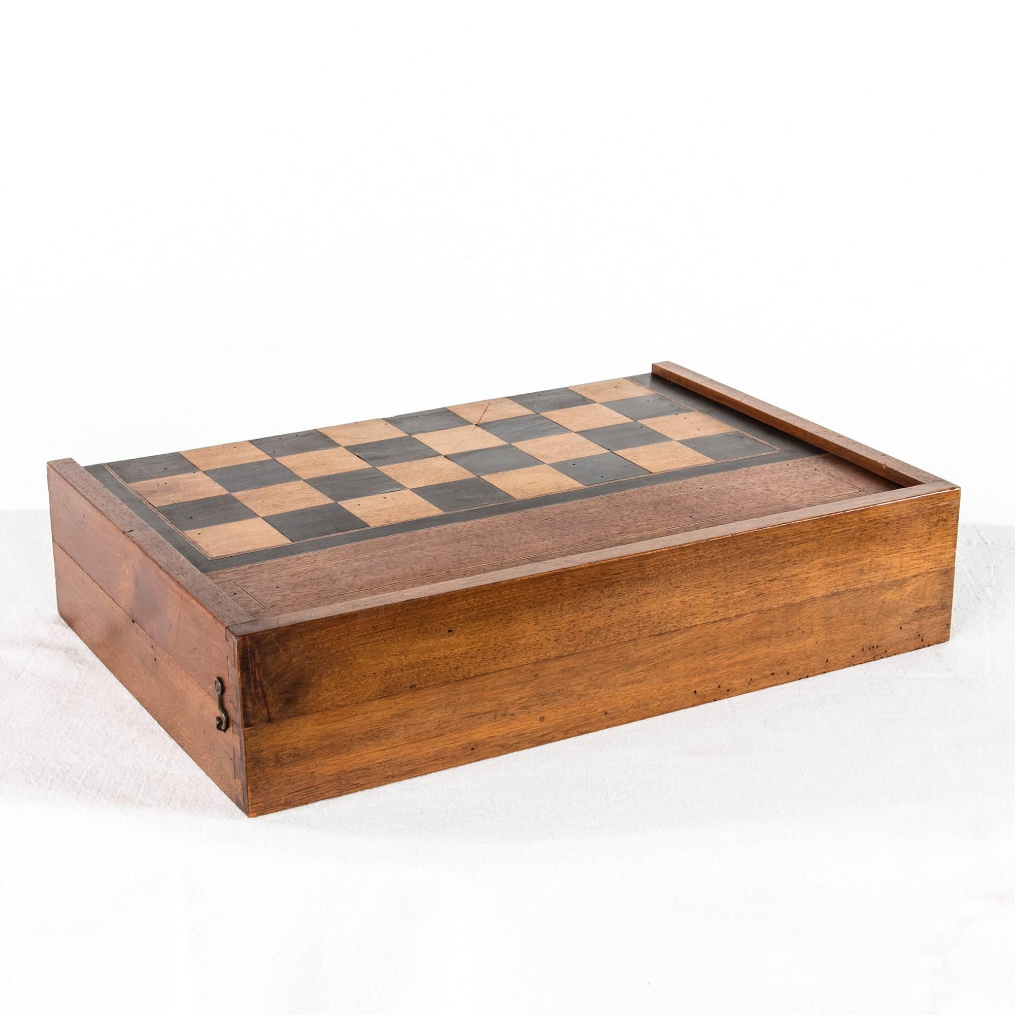 An artisan made, circa 1900 game board and box, this piece is meant for checkers, chess, or backgammon. Complete with leather cups, a set of wooden game pieces, and two pairs of dice, this large game surface closes to make an elegant tabletop box