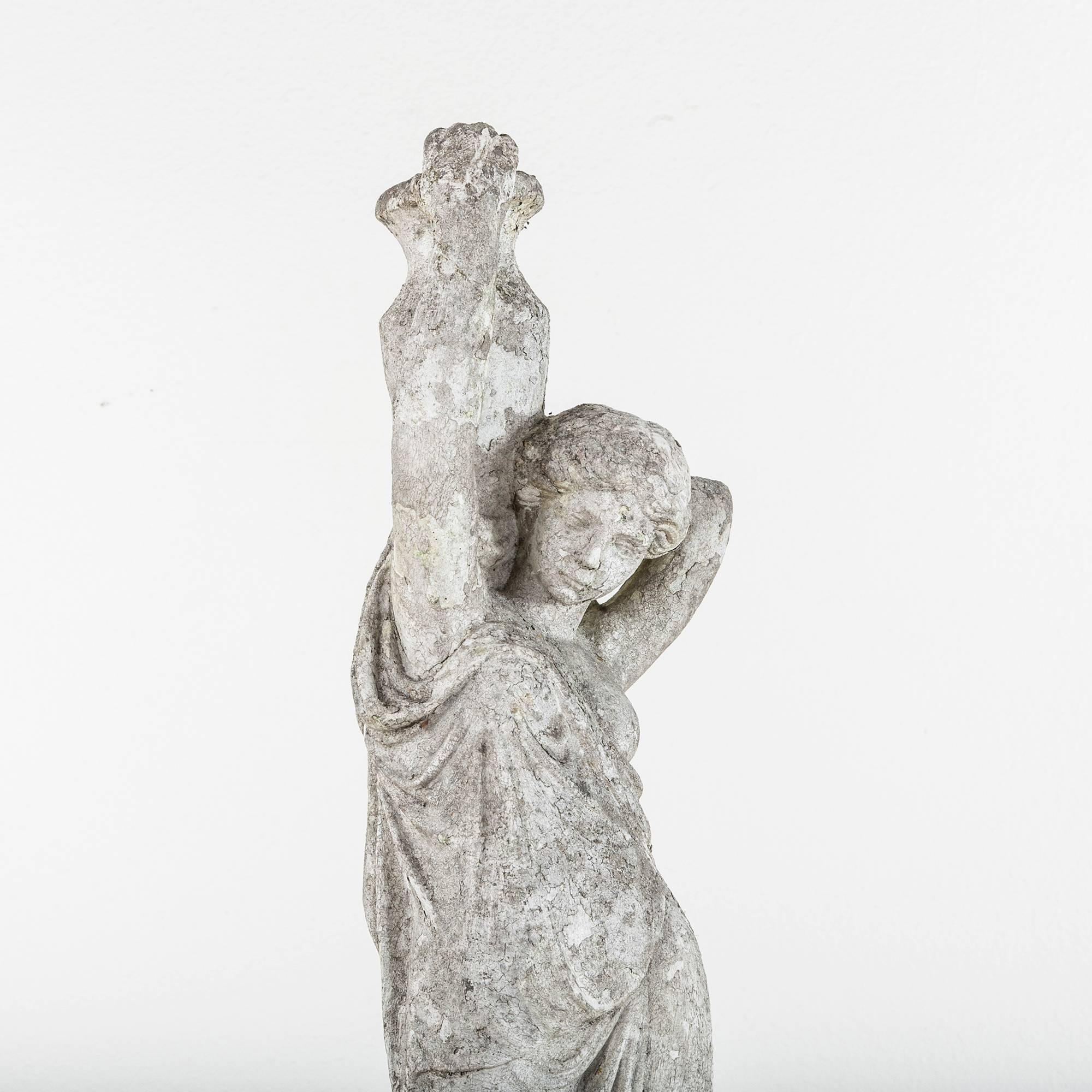 This beautifully aged stone statue reflects the Classical Greek style. The figure of a female stands holding a large urn for water over her shoulder. With the lovely patina only age and weathering can bring, this elegant statue will make a divine