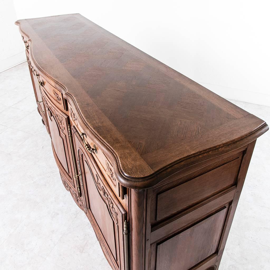 This elegant Louis XV style French oak enfilade features three doors and drawers with a bow front center and a parquet top. Its hand-carved doors are beautifully detailed with a simple shell motif repeated in the lower apron. Its brass hardware