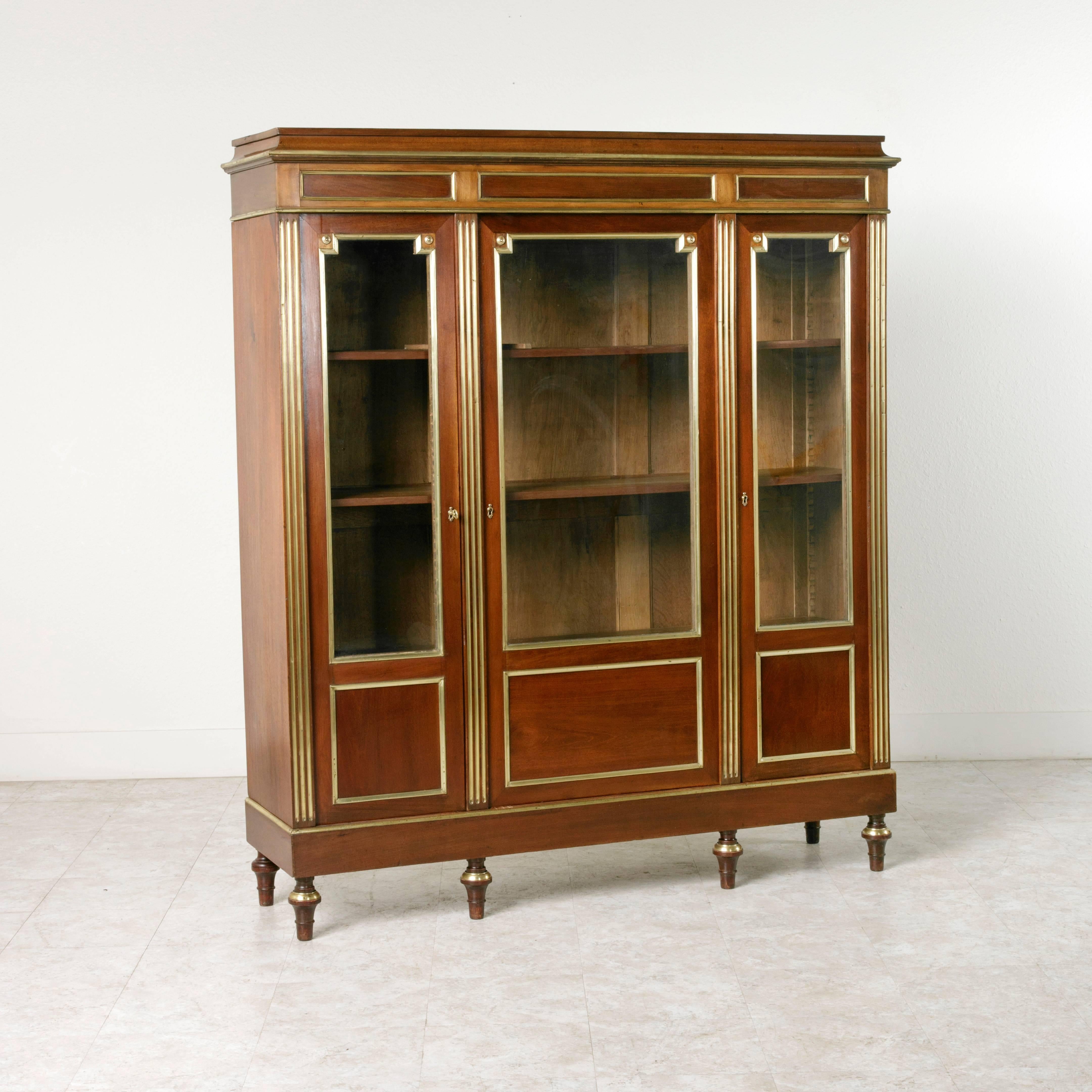 This incredibly finely detailed Louis XVI style mahogany bibliotheque 
has been created by hand to the highest level of craftsmanship with bronze inlay and banding carried up its four fluted column faces, across its three inset doors, and even