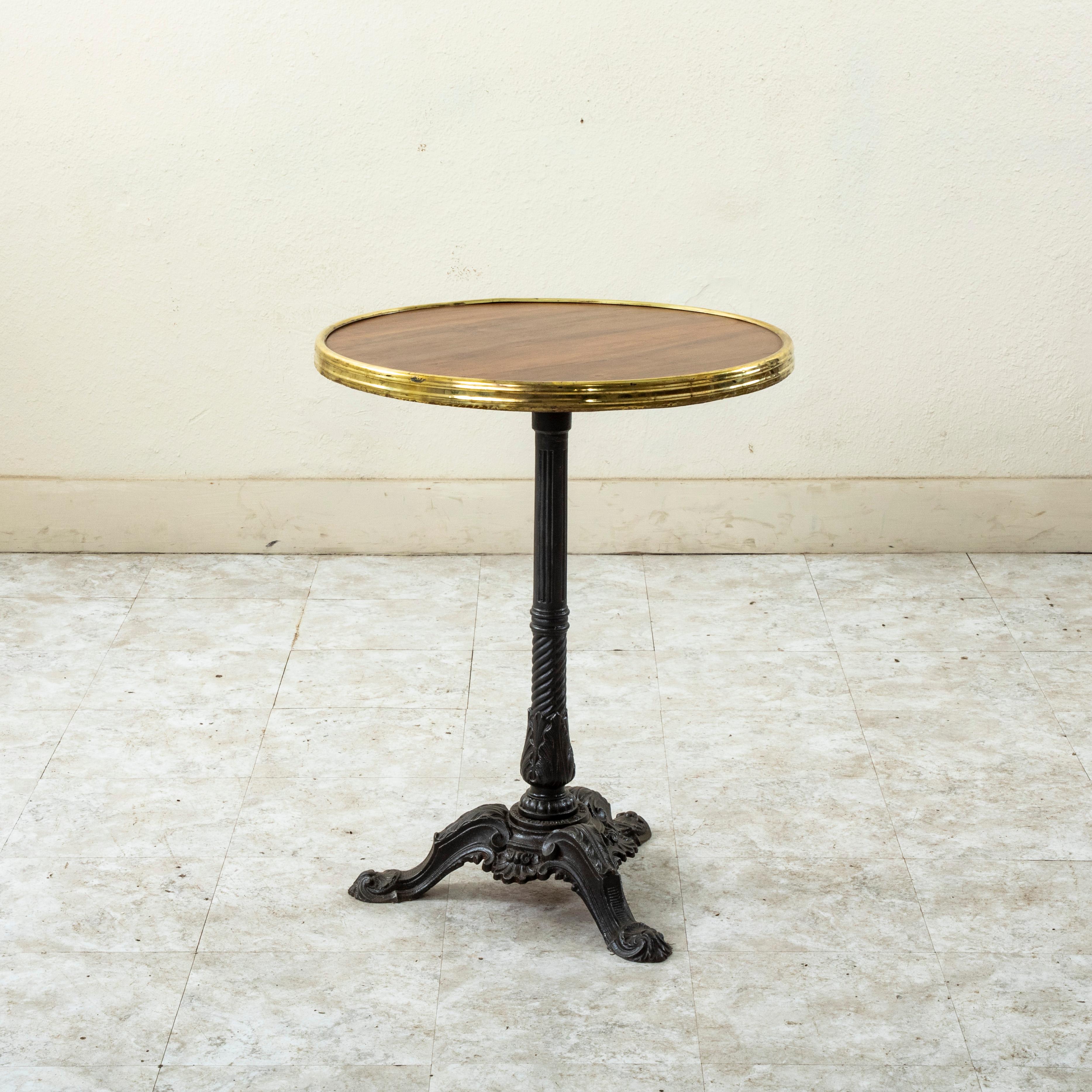 Cette table de bistrot ronde française du début du XXe siècle est dotée d'un socle en fonte et d'un plateau en peuplier garni de laiton. Des enroulements, des feuilles d'acanthe et des coquillages détaillent la base du trépied. La base est marquée