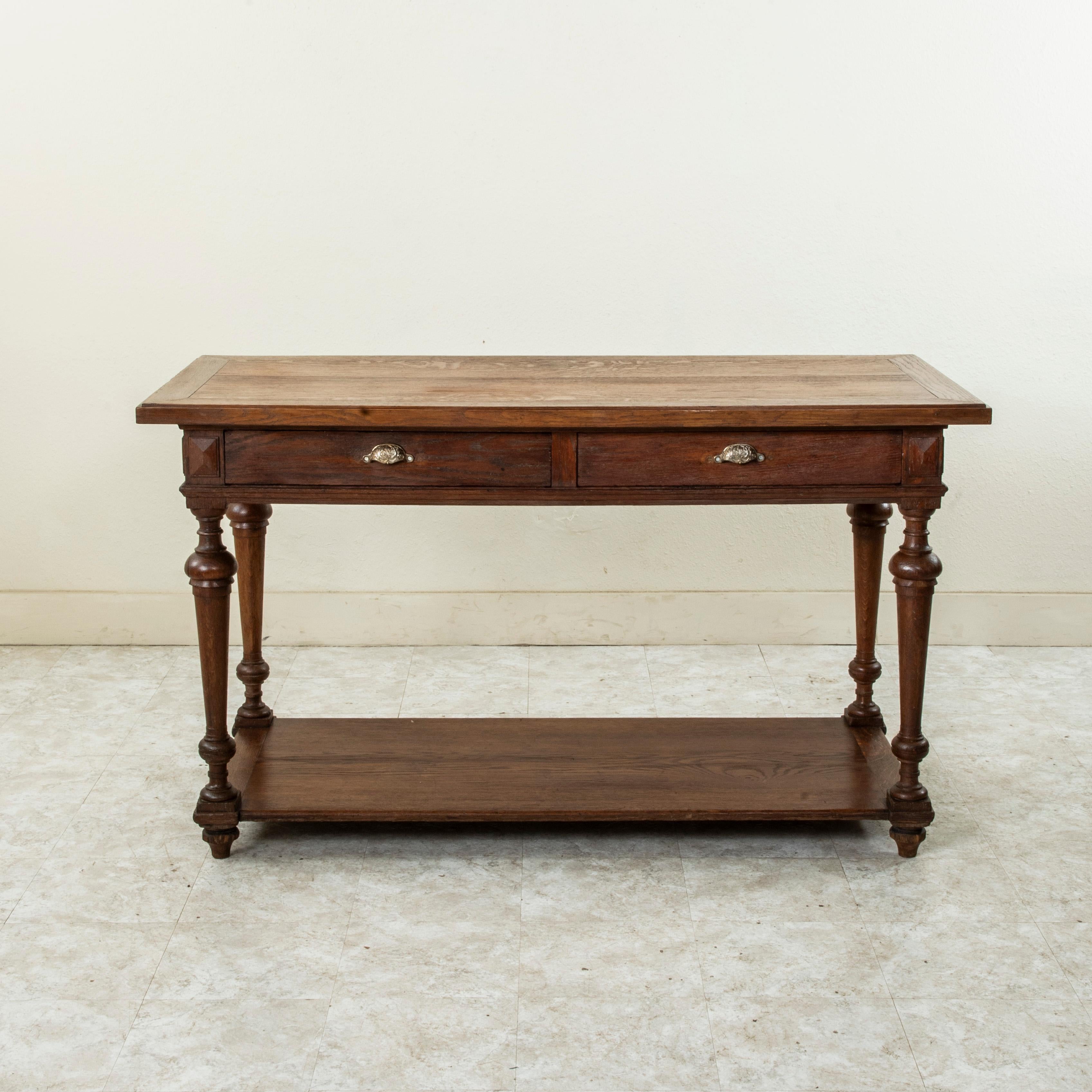 Utilisée à l'origine dans un magasin de tissus français pour étaler et couper les tissus au début du XXe siècle, cette table de marchand de soie en chêne repose sur des pieds tournés effilés qui soutiennent son étagère inférieure. Deux tiroirs à