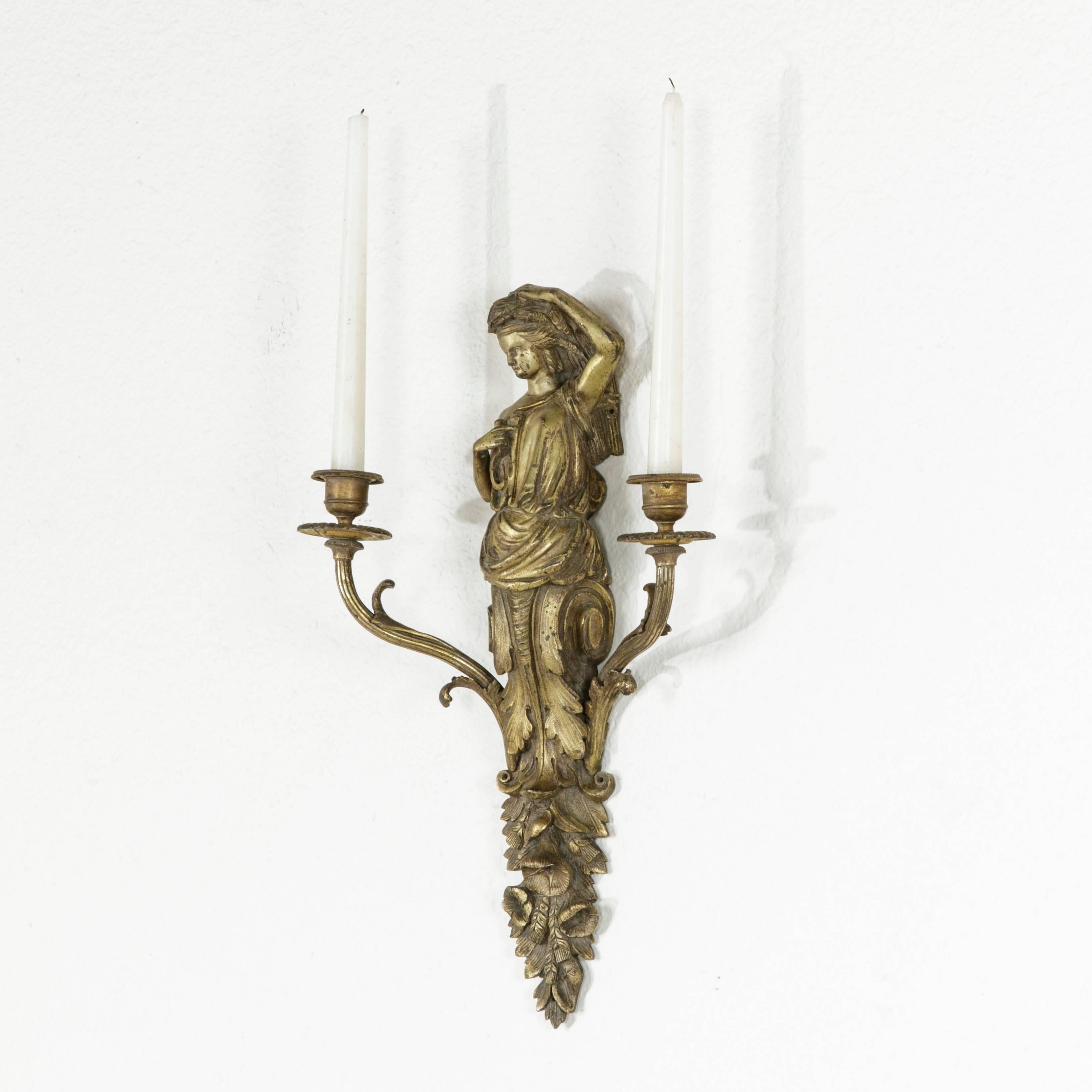 This Napoleon III period bronze sconce features a classical female figure standing atop curling acanthus and flowers. Two candle arms extend from the floral base. The unusual large size of this piece paired with its intricate solid bronze