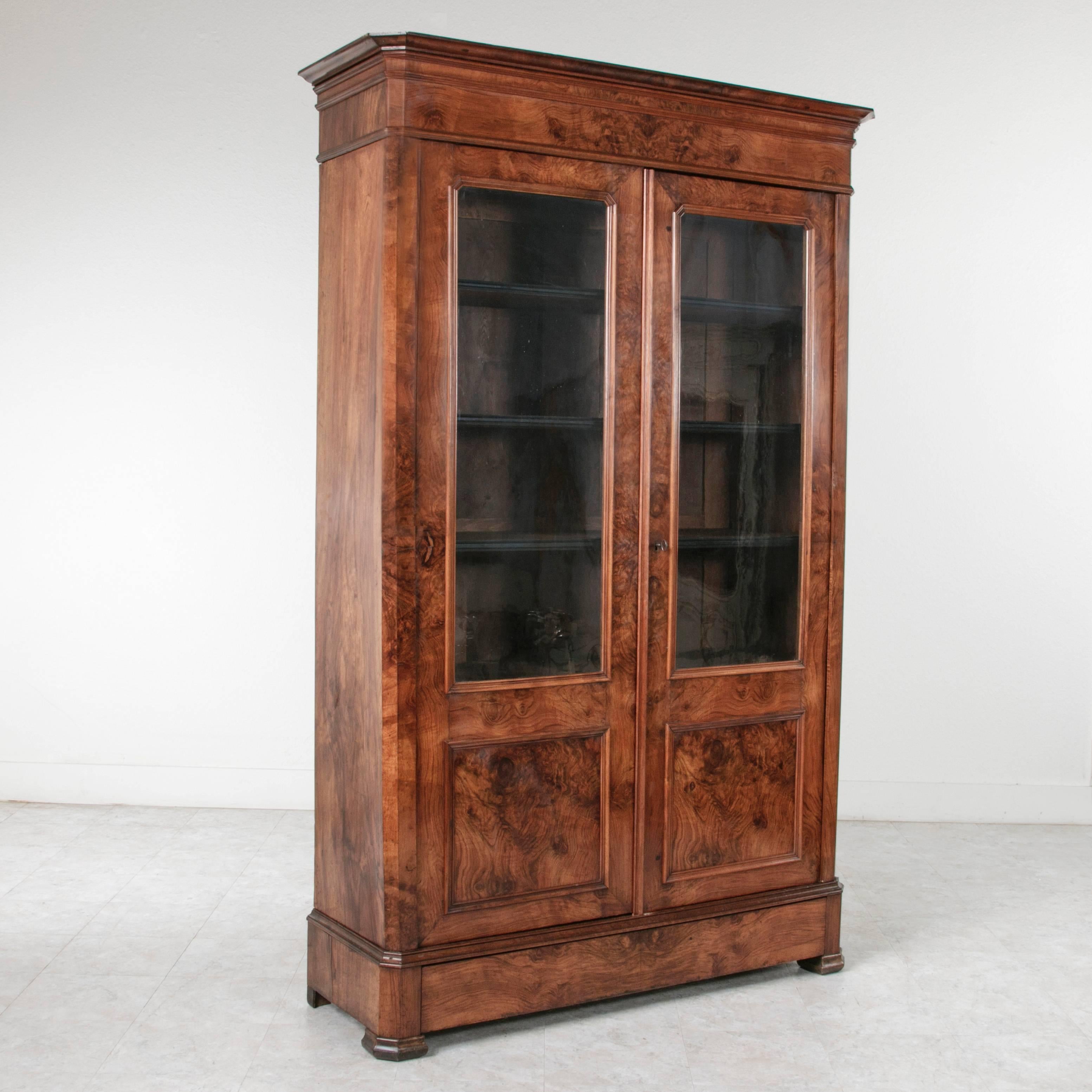 This exceptional bookmatched walnut Louis Philippe period bibliothèque features a hidden lower drawer and original handblown glass doors. The intricate burl of this piece continues up its smooth sides and is carried across the trim at the crown and