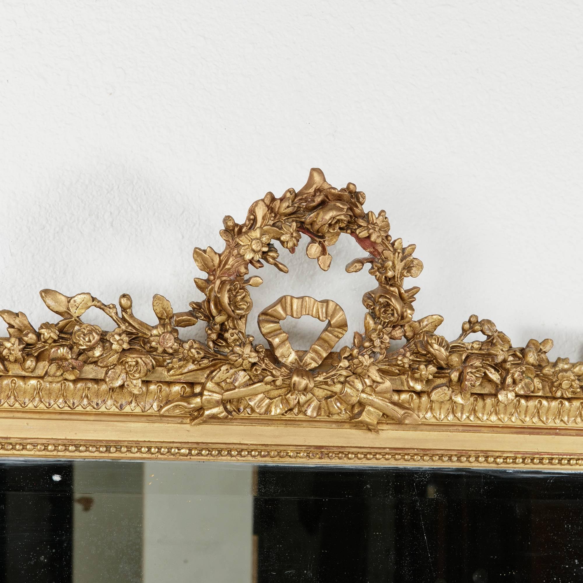 This exquisite 19th century hand-carved giltwood mirror is a quintessential example of the Louis XVI style. Its frame features classic Louis XVI motifs in its rows of finely carved leaves, beading, and corner rosettes. A delicately hand-carved