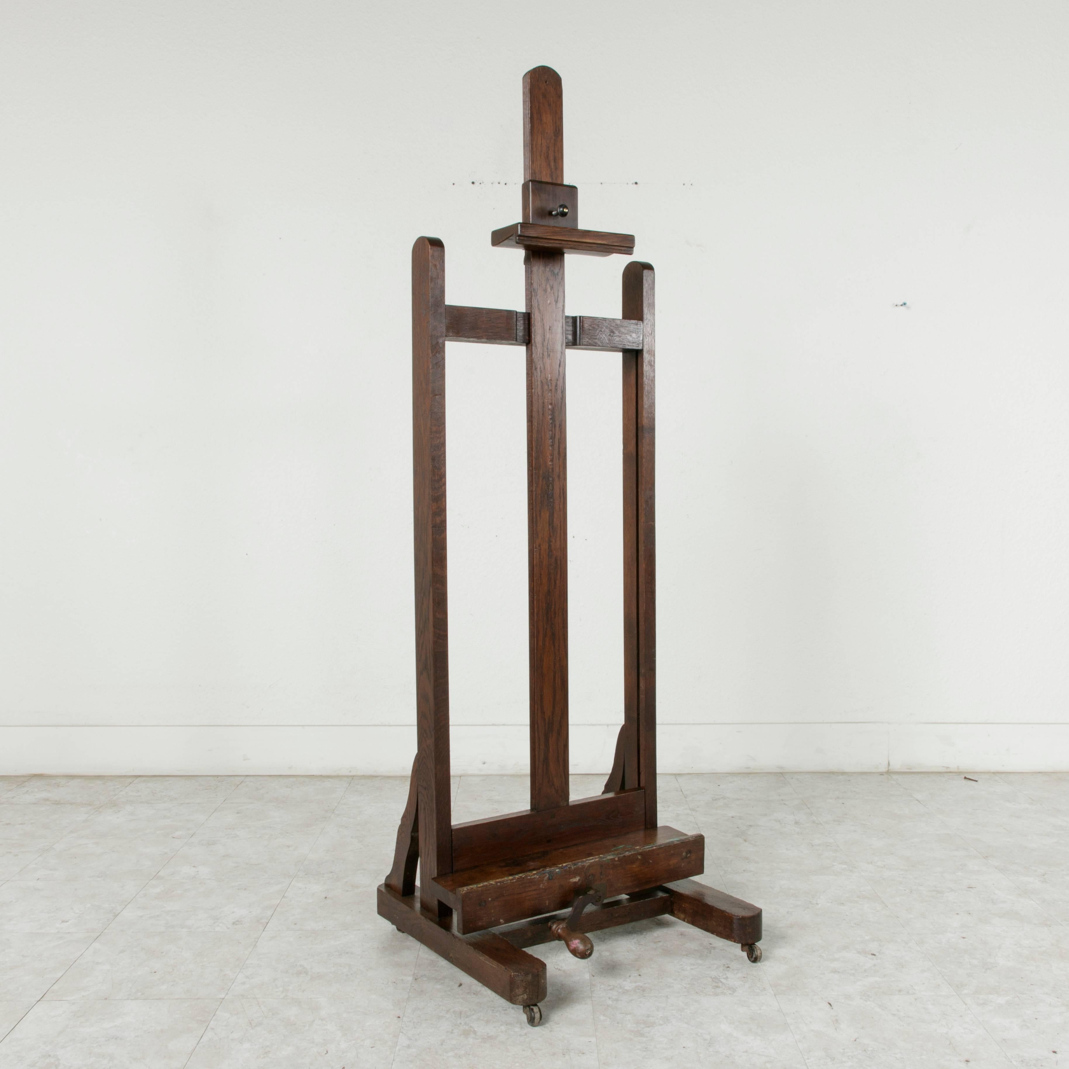 This grand early 20th century oak artist's easel has its original functioning crank mechanism to adjust the tray height. With an adjustable height of 64 inches to 96 inches, this sturdy easel can handle impressively large canvases or make an