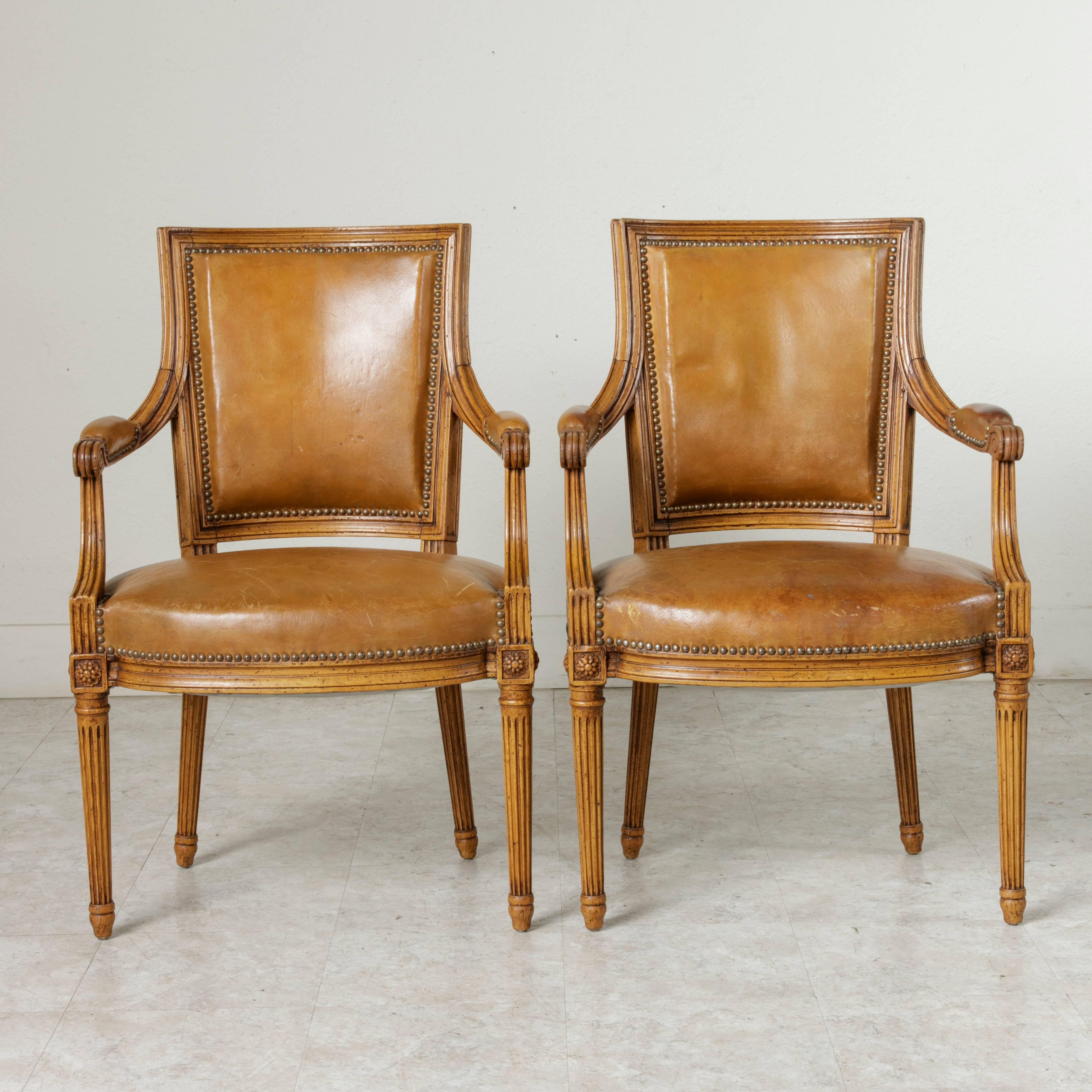 Made by Great Britain's Mayfair of London, this Mid-Century pair of Louis XVI style beechwood armchairs features Classic fluted legs, rosettes on the die joints, and scrolled armrests. A sturdy hand pegged construction lends stability to this Fine