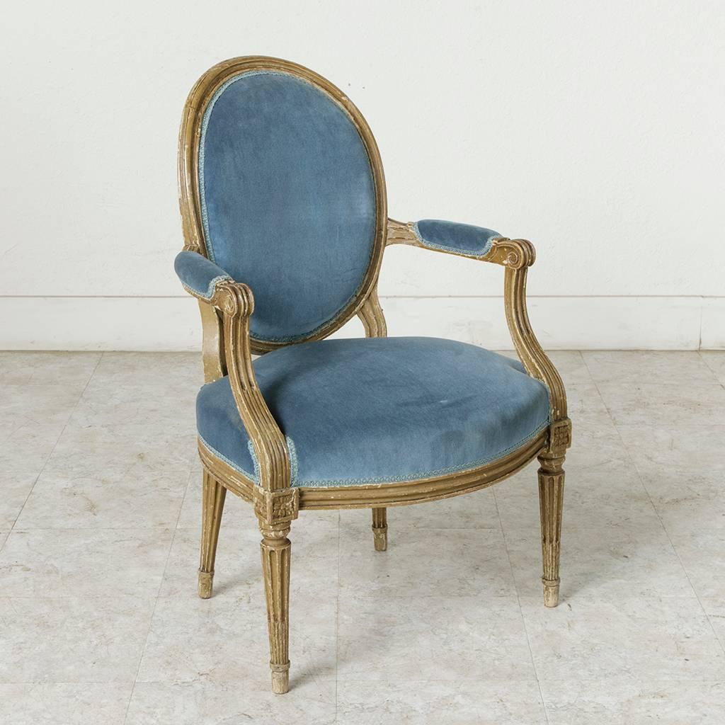 Found in a parsonage in Normandy, France, this pair of Louis XVI period cabriolet armchairs are finished in their original patination. This classic pair features medallion backs, fluted arms with scrolled armrests, and tapered legs of cabled