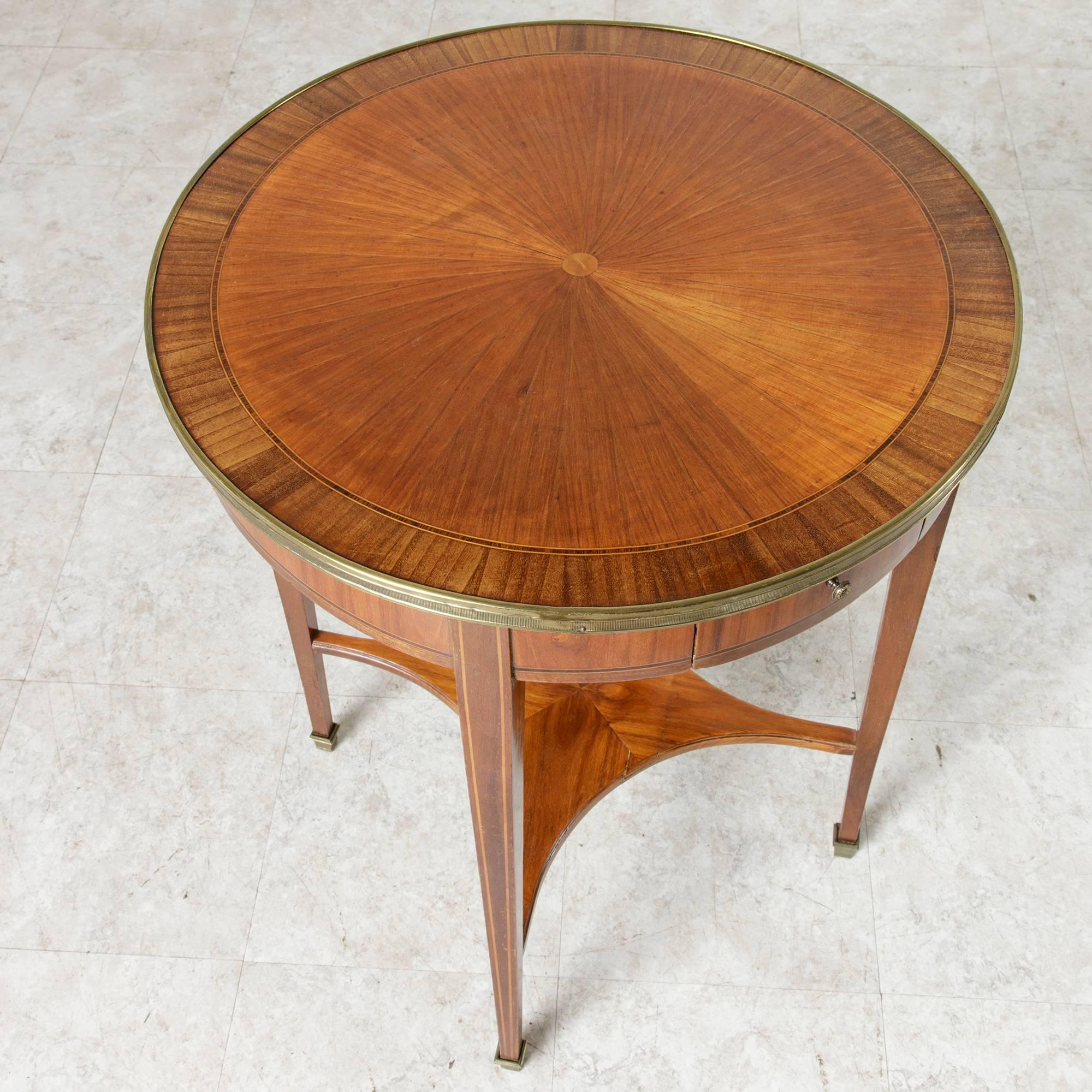 This Art Deco period gueridon or side table in the Louis XVI style features an inlaid rosewood and walnut marquetry top in a sunburst pattern. Bands of palisander and sycamore form fine lines on its tapered square legs and around its apron. A brass
