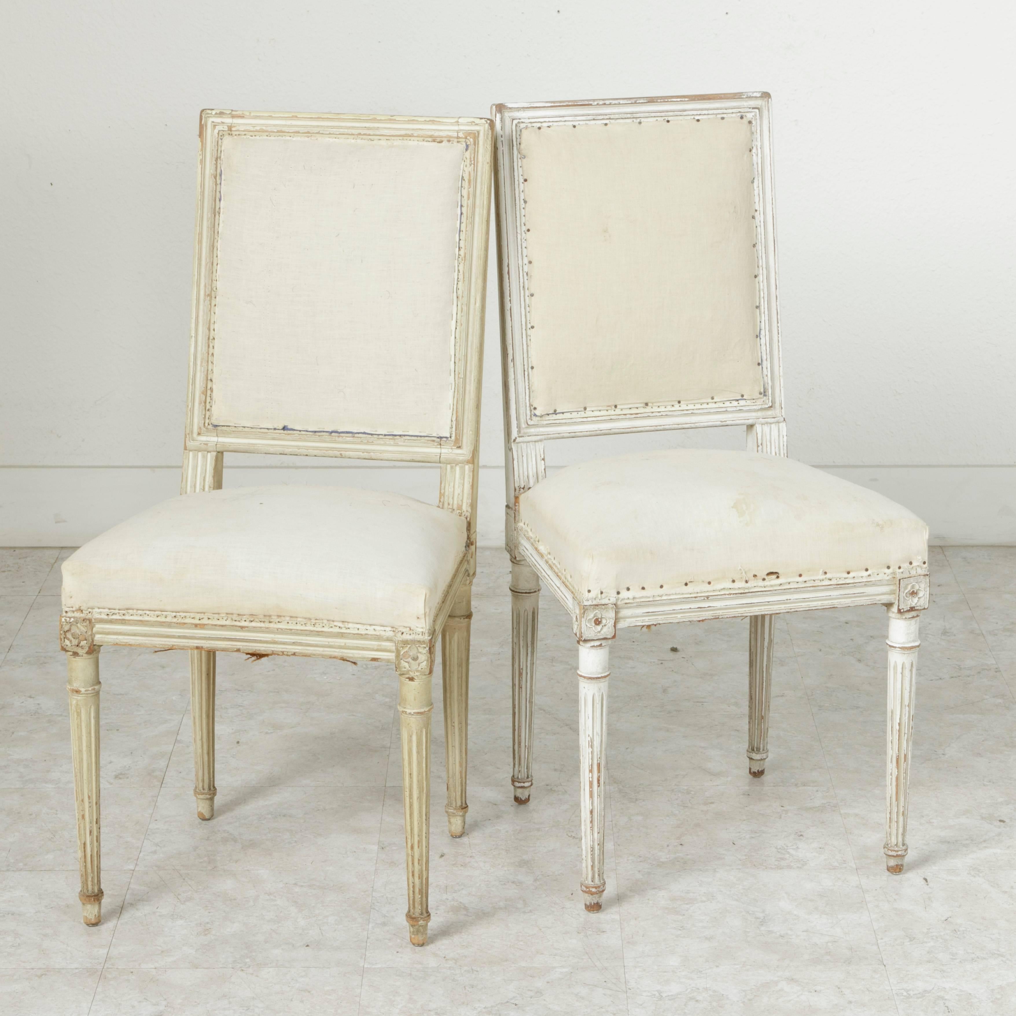 This set of four late 19th century hand-carved and white painted Louis XVI style side chairs of hand pegged construction features carved rosettes on the die joints and classic tapered fluted legs. The natural wear of the patina lends a weathered