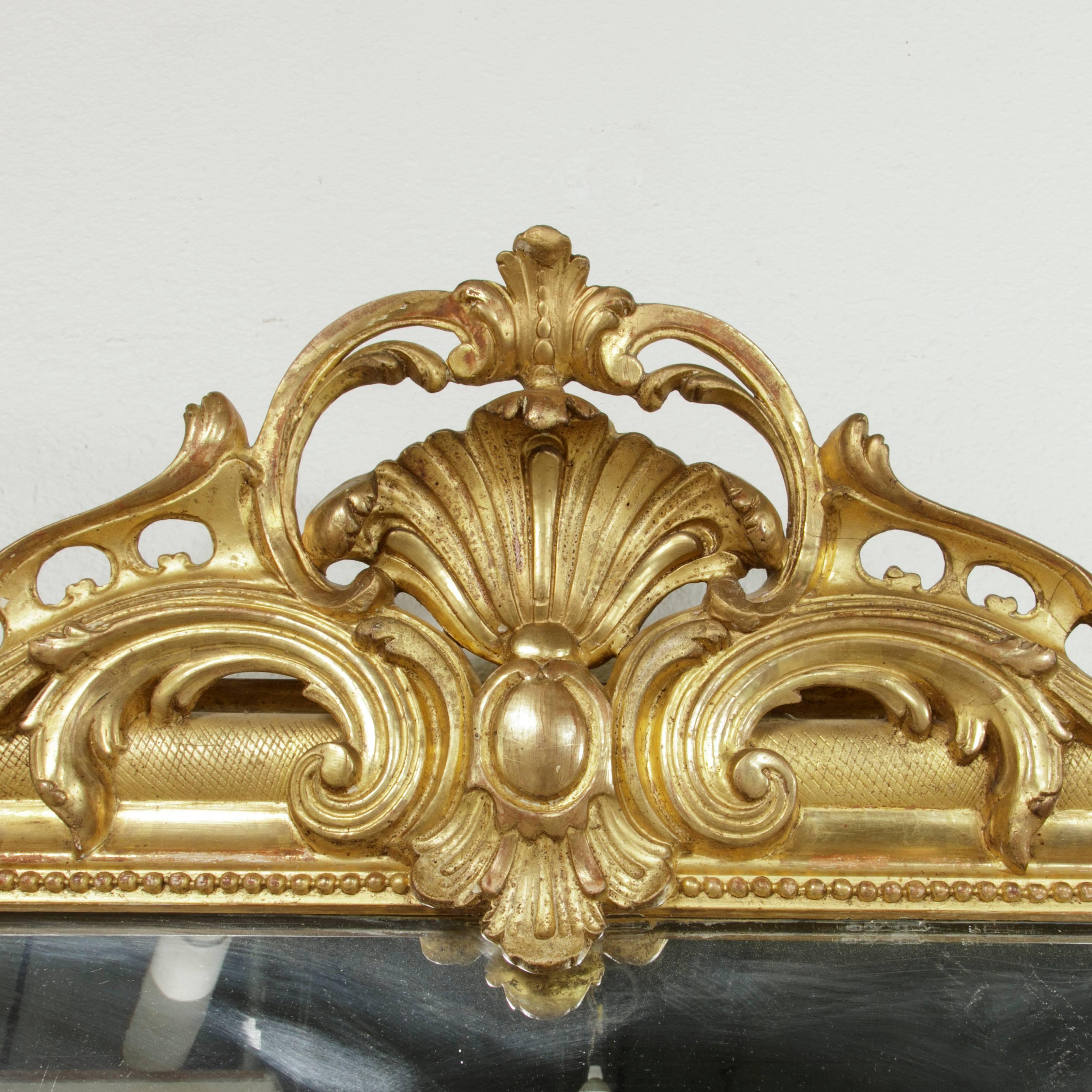 This 19th century French giltwood mirror features a classic Louis Philippe frame crowned with a central Regency style cartouche and gadrooning flourish. Beading along the inside edge of the frame and an incised leaf pattern lend additional detailing