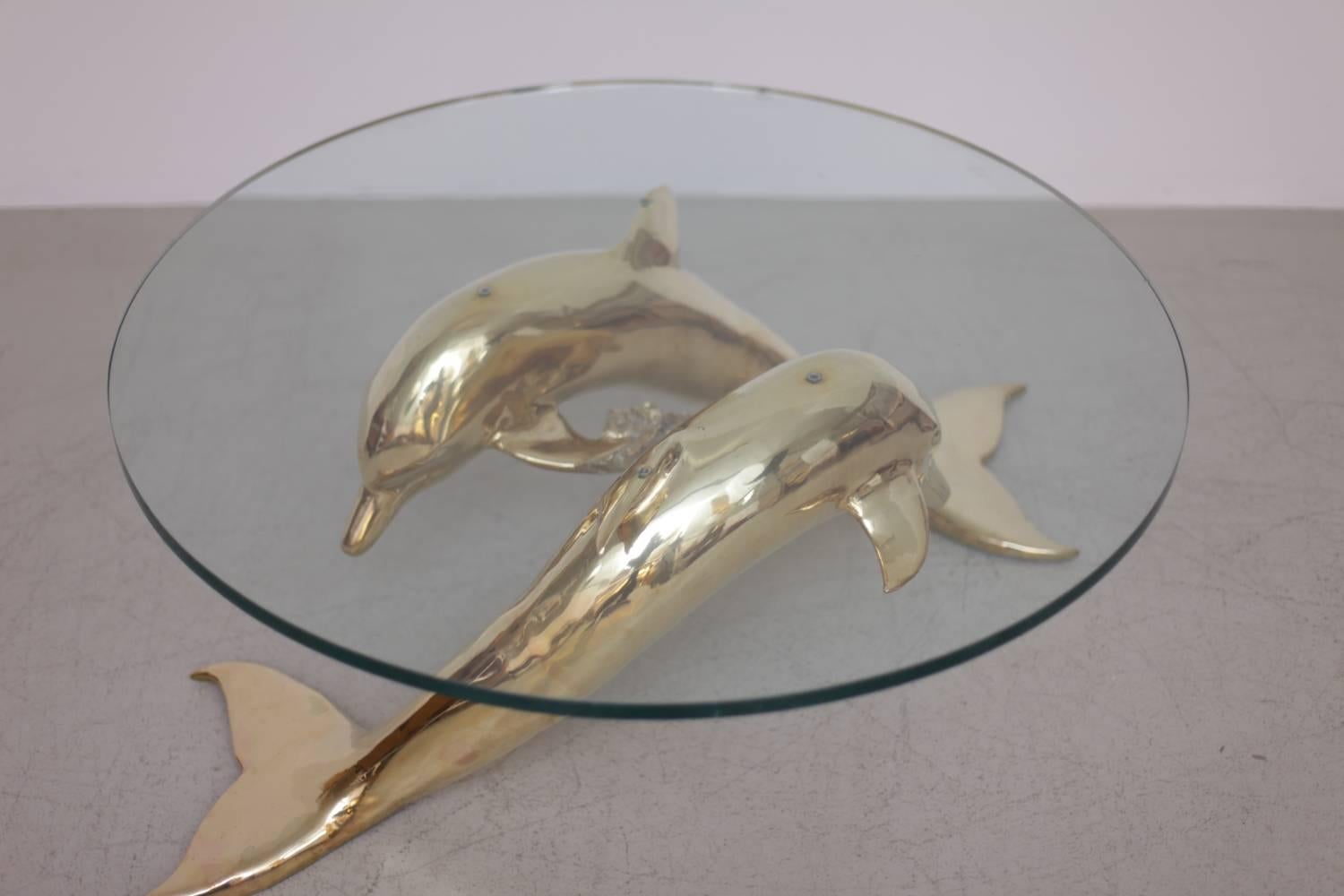 Very elegant and huge coffee table in brass and glass. The glass table top is holded by two brass dolphins. The table is a really eyecatcher. The glass top is chipped. The brass is in excellent condition.

