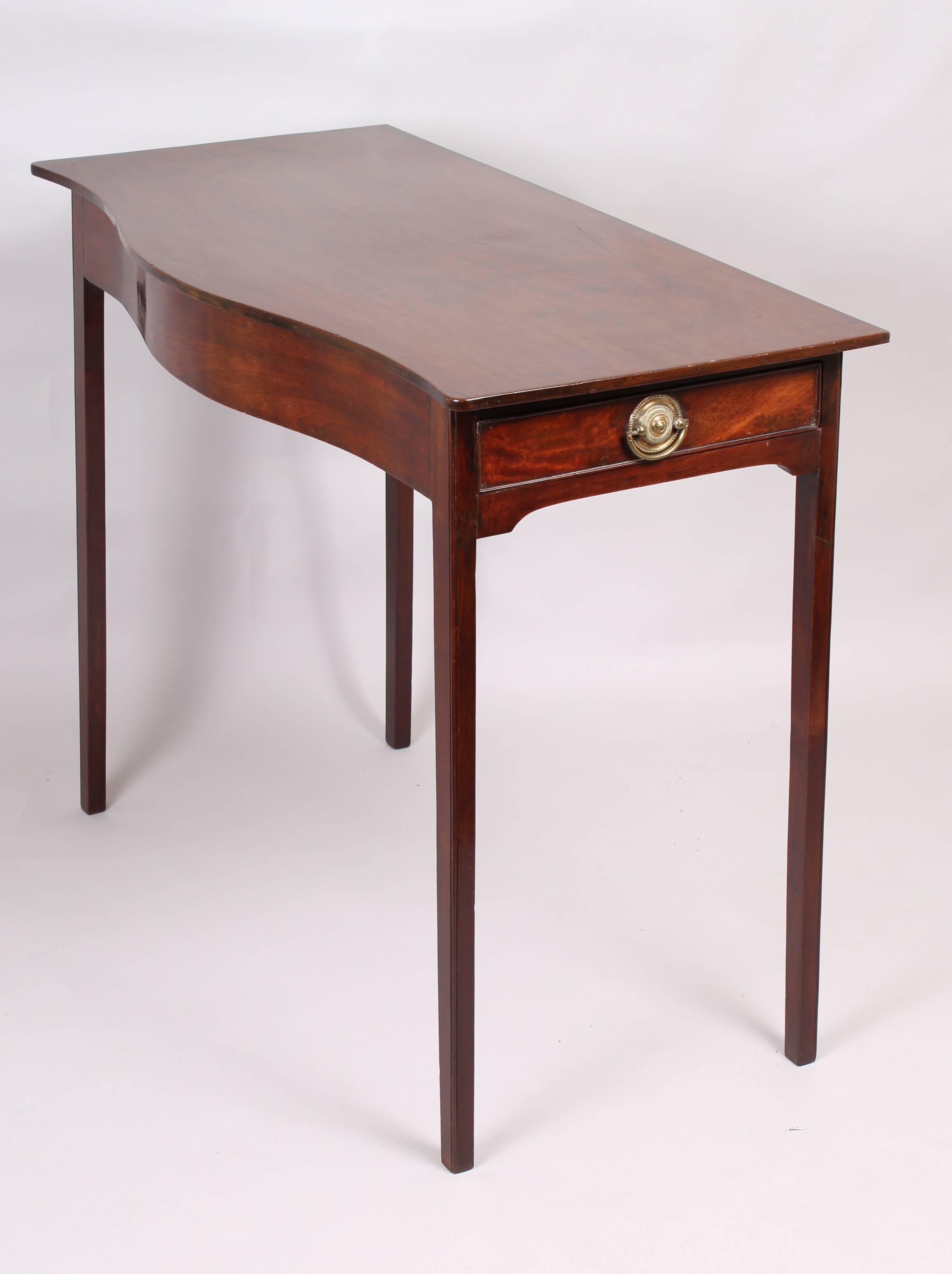 George III period mahogany side table of simple serpentine form; the overhanging top on a frame with an oak-lined drawer fitted in the right-hand side.