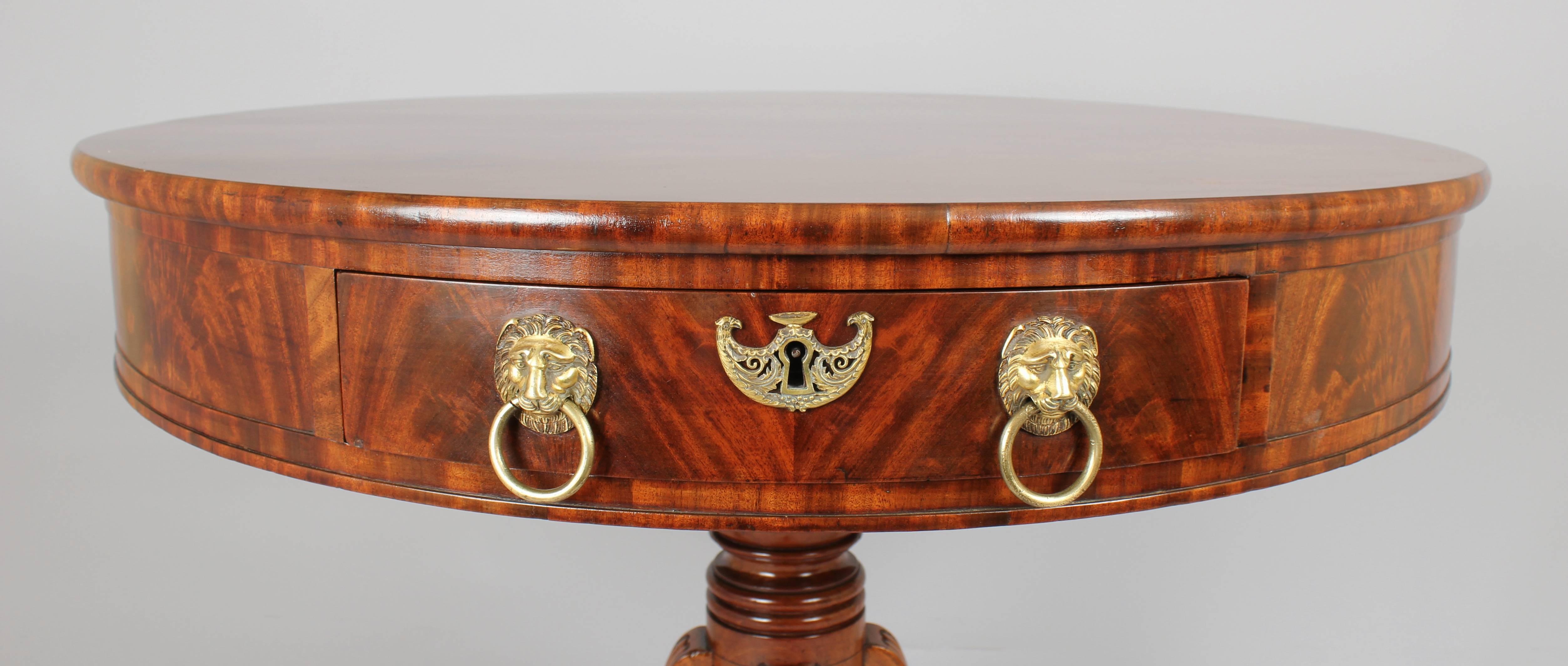 Fine quality early 19th century Continental mahogany small drum-table with richly-figured and matched flame veneers throughout; the two drawers with original cast-brass lion's-mask handles and pelta-shaped escutcheons, one fitted with a hinged