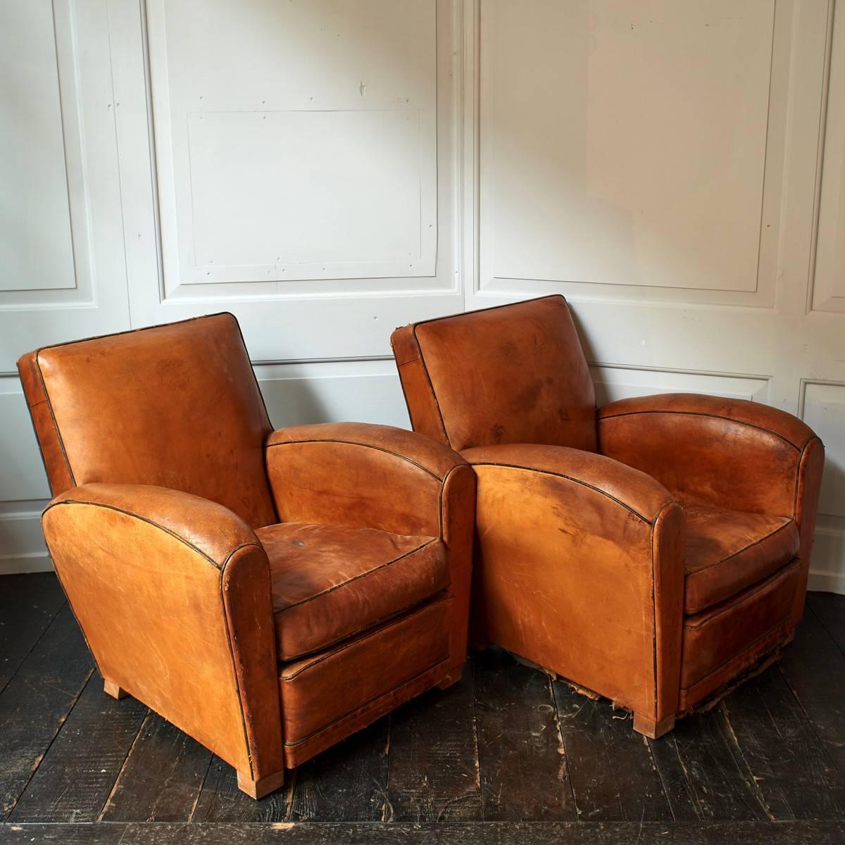 Fauteuil confortable of French origin. The distressed, soft leather chairs feature small tears and rips as you would expect from a pair of chairs of this age. Springs loose underside.