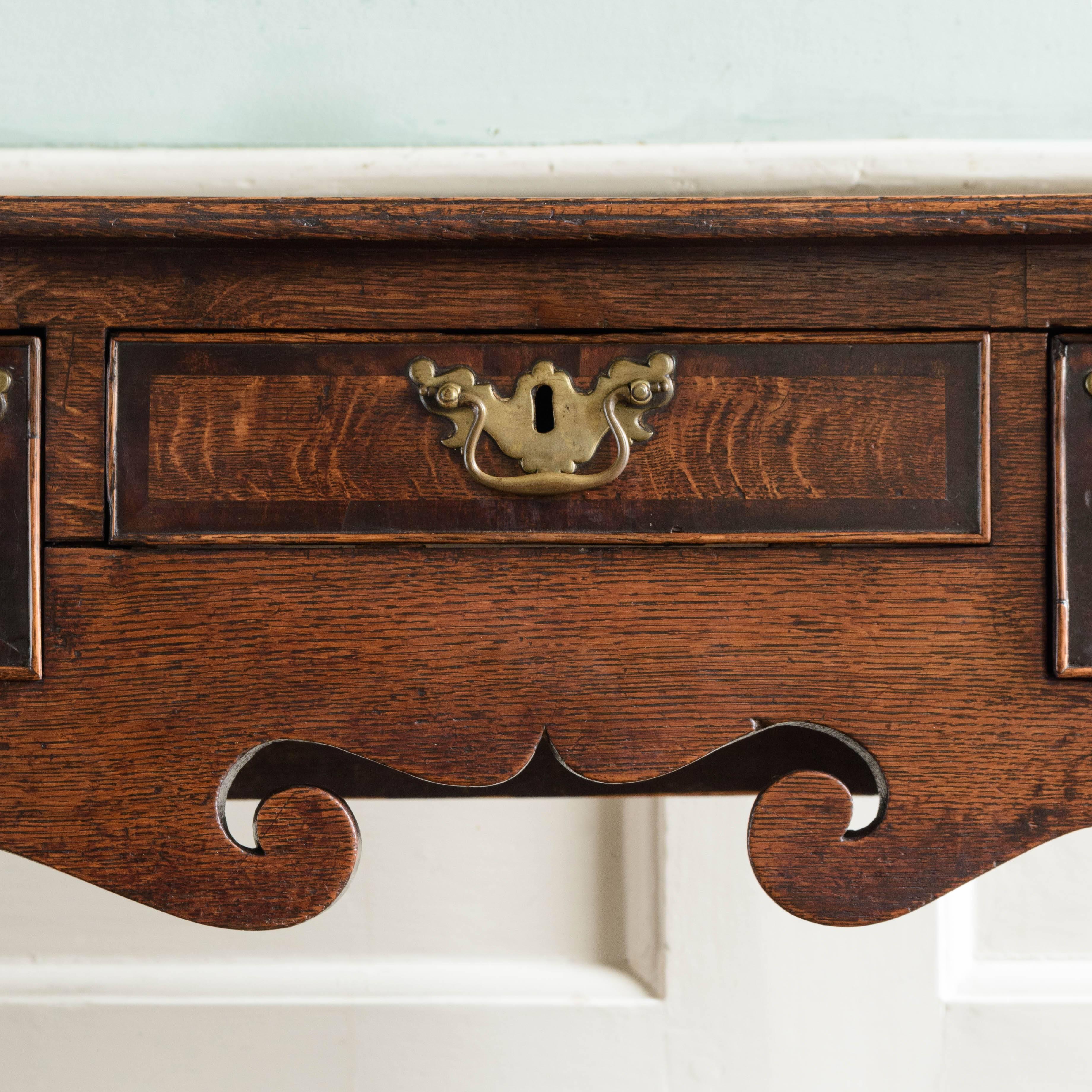 George II oak lowboy, the well figured moulded edge top above three walnut cross-banded drawers with shaped frieze below on cabriole legs with pad feet.