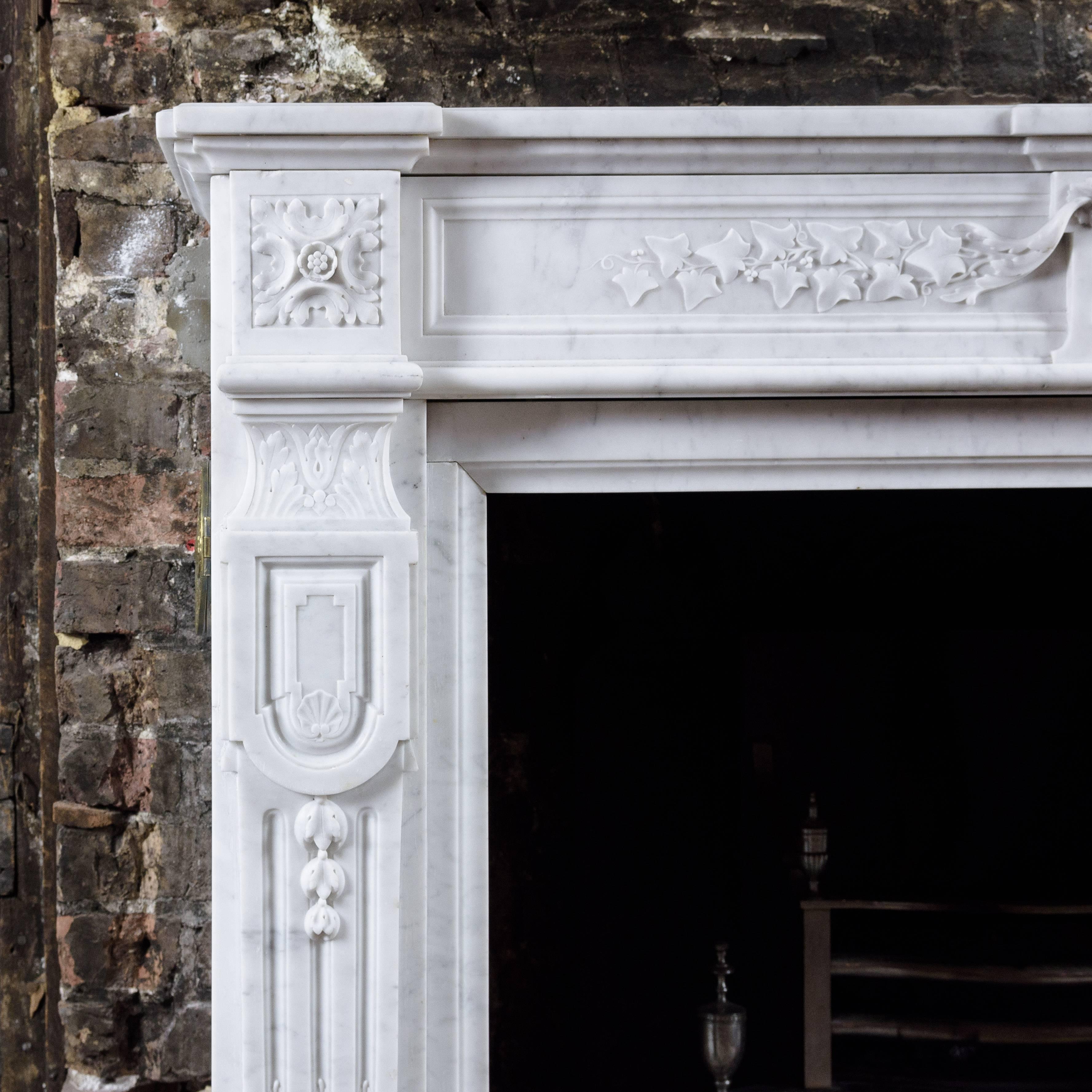 French 19th century Carrara marble chimneypiece, in the Louis XVI style, the breakfront moulded shelf above frieze centred by a garland of flowers, flanked by trails of ivy leaves with endblocks of square paterae to either side, the stop-fluted