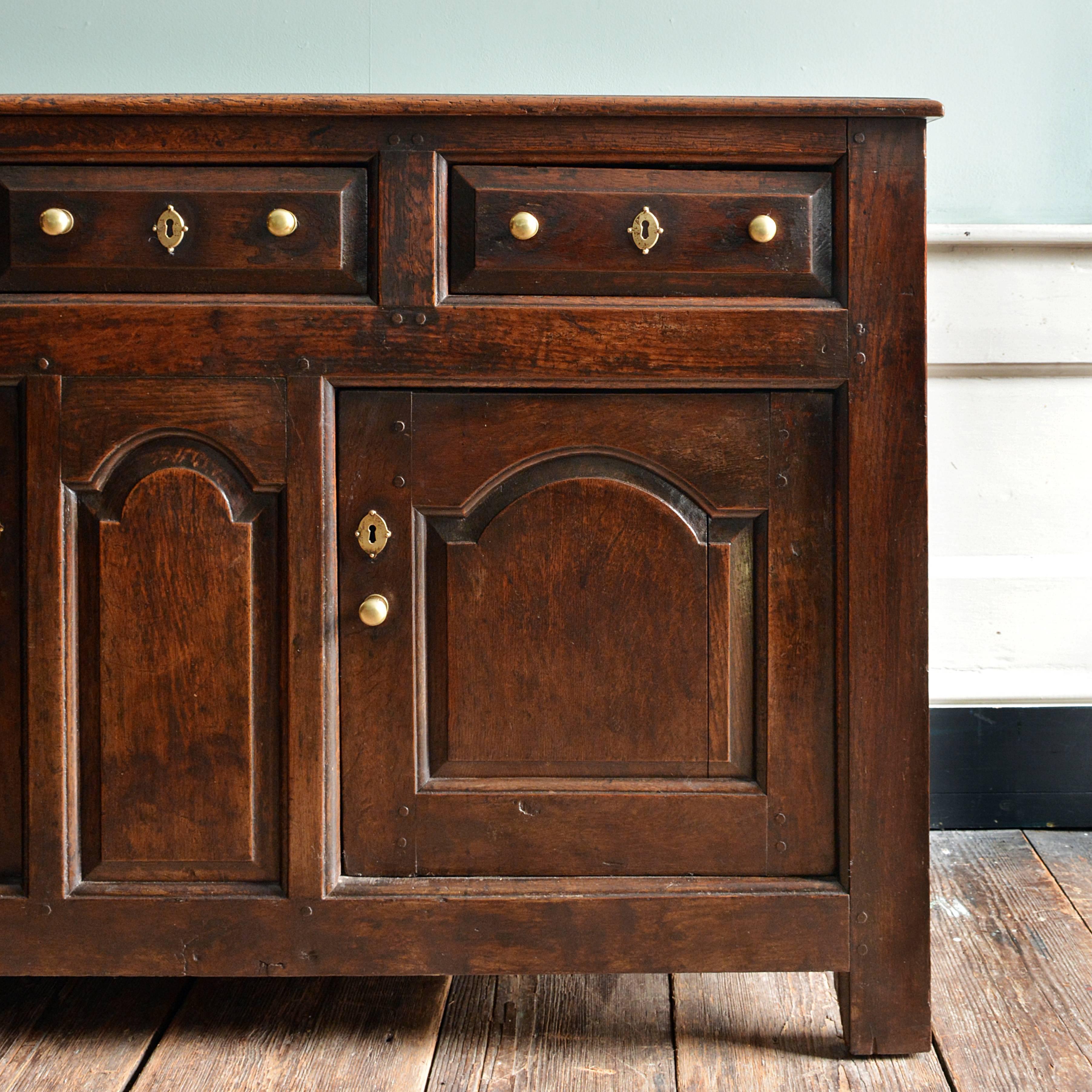 A George II oak dresser base, circa 1730, Caernarfonshire, North Wales, the three fielded drawers over central arch arched fielded panel flanked by a pair of arch fielded cupboards, on stile supports. Excellent color and patination
