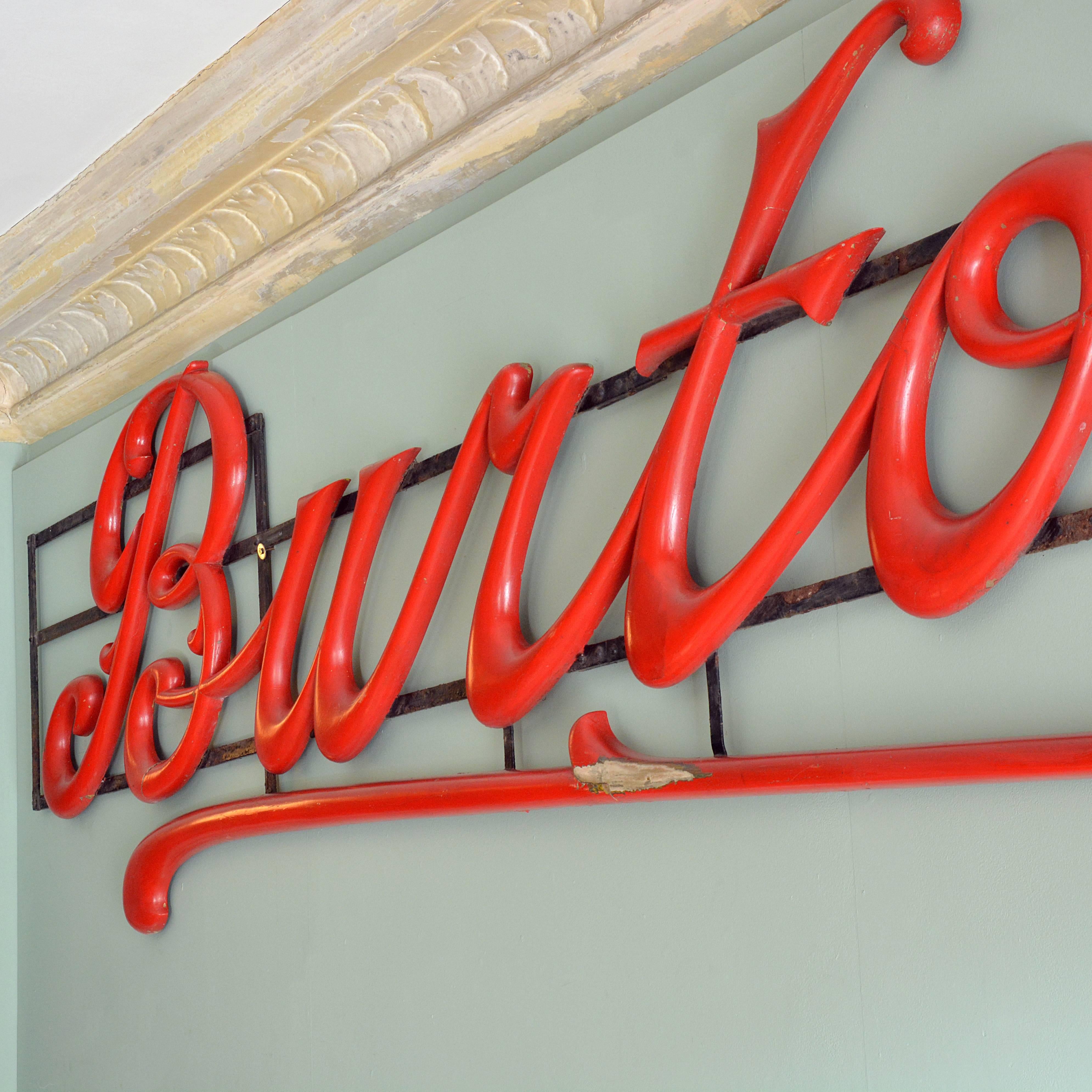 A large carved timber 'Burton's' serif-script shop sign, mounted on iron frame. Old red paint over original gilt finish.

Available to view at Brunswick House, London.

Dimensions: 403cm (158¾") wide, 90cm high, 6cm (2¼") deep.
 